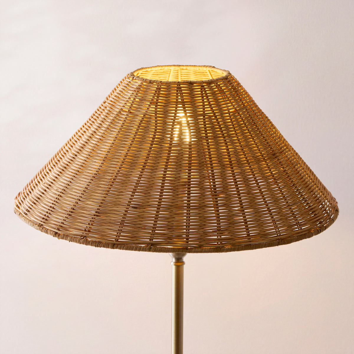 Close up of the Endon Arlo floor lamp's hand crafted brown rattan shade lit from inside, antique brass stem below