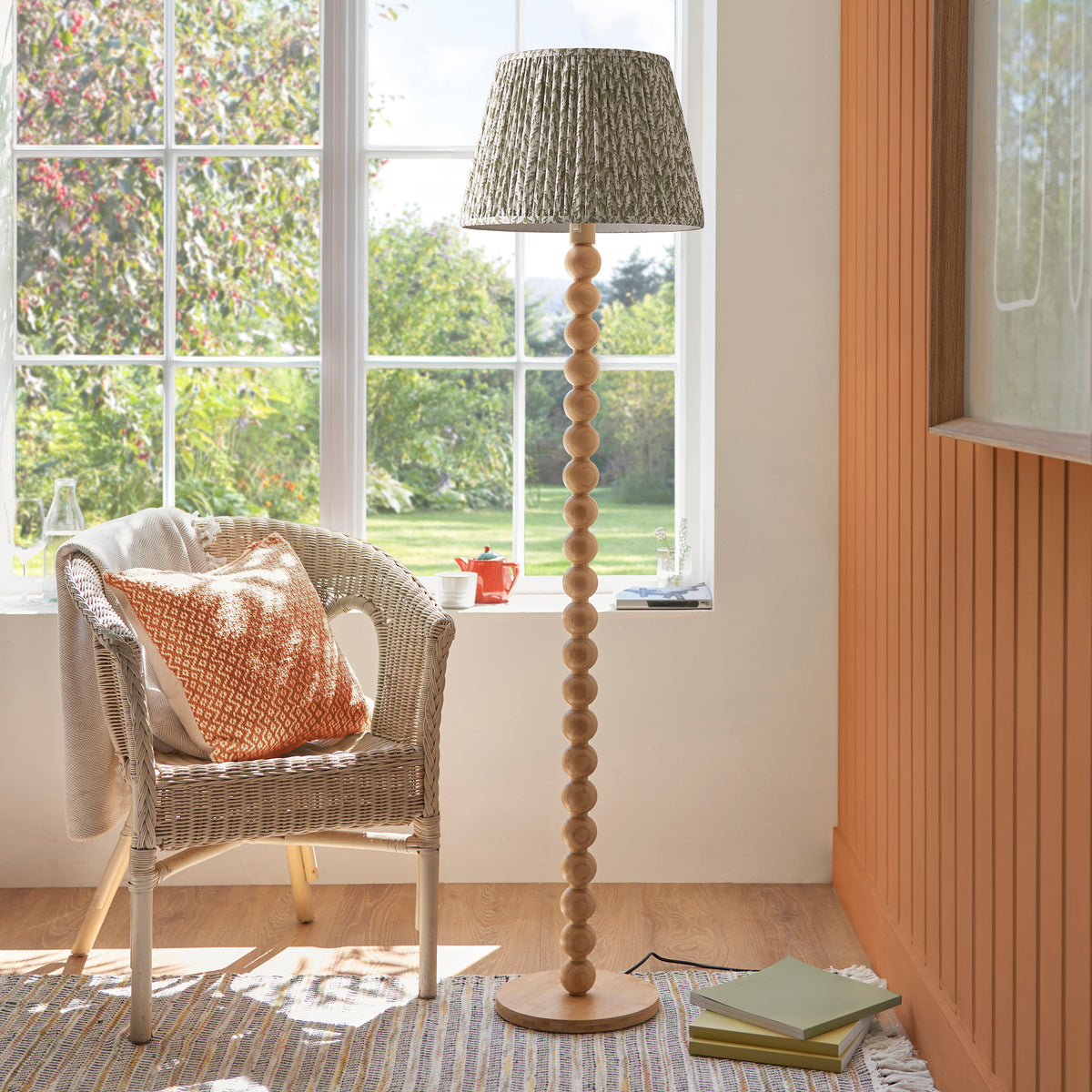 Endon Cane floor lamp unlit in a living room with a wicker armchair, striped rug and books, showing the herb garden green leaf print shade