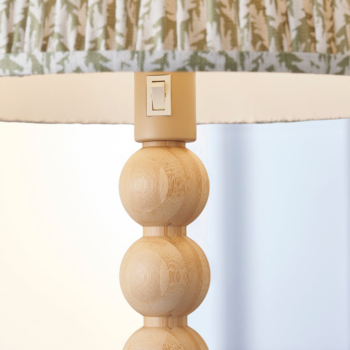 Close up of the Endon Cane floor lamp lit, showing the rocker switch on the lamp holder, the top bamboo spheres and the green leaf shade edge