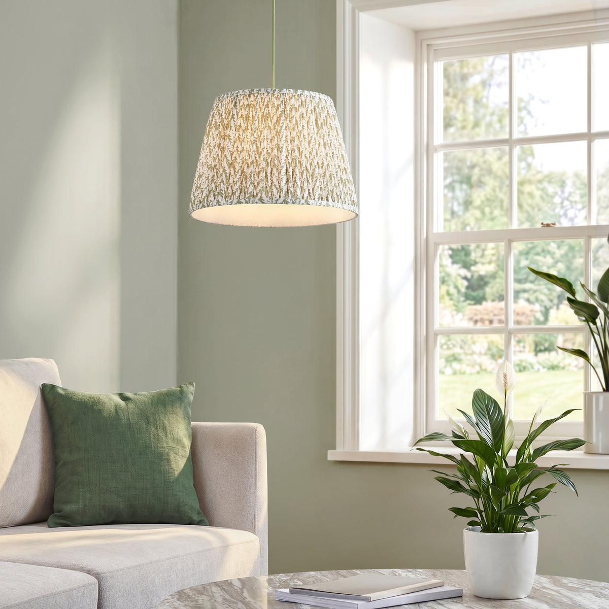 Endon Eltham and Leaf pendant light lit in a living room with a cream sofa, green cushion, sash window and peace lily plant