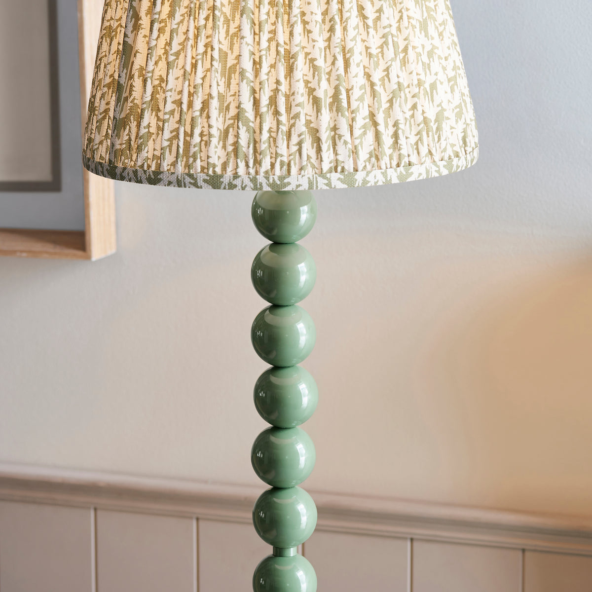 Close up of the Endon Higgledy floor lamp lit, lower edge of the pleated leaf print shade above gloss Cotswold green spheres