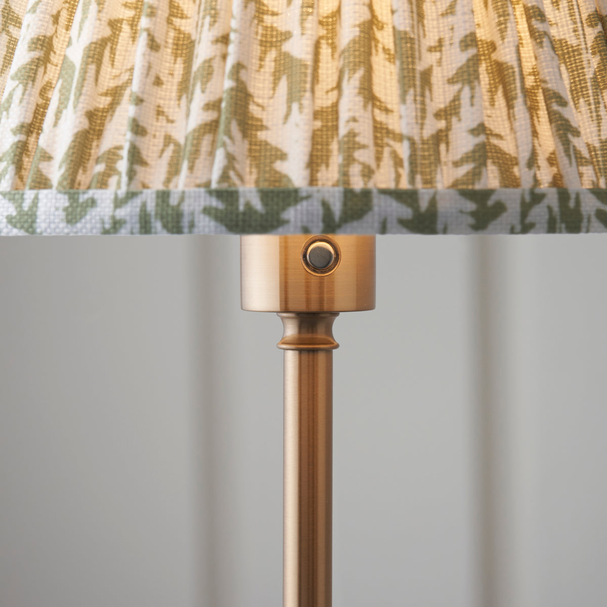 Close up of the lit herb garden green pleated leaf shade and brushed aged brass lamp holder with touch dimmer button on the Endon Burley floor lamp