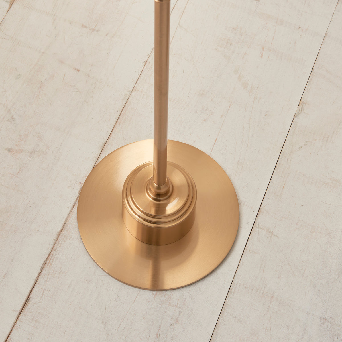 Close up of the round brushed aged brass base of the Endon Burley floor lamp standing on white painted floorboards