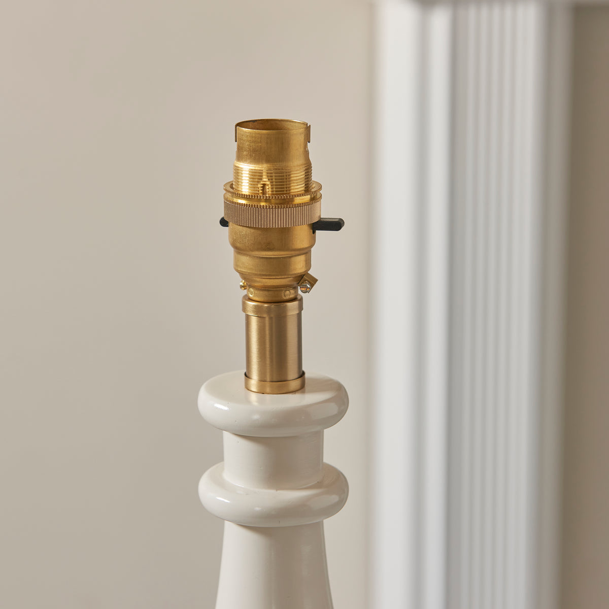 Close up of the switched brass B22 lamp holder on the Endon Myrtle table lamp, unlit, gloss almond white column below, cream wall behind
