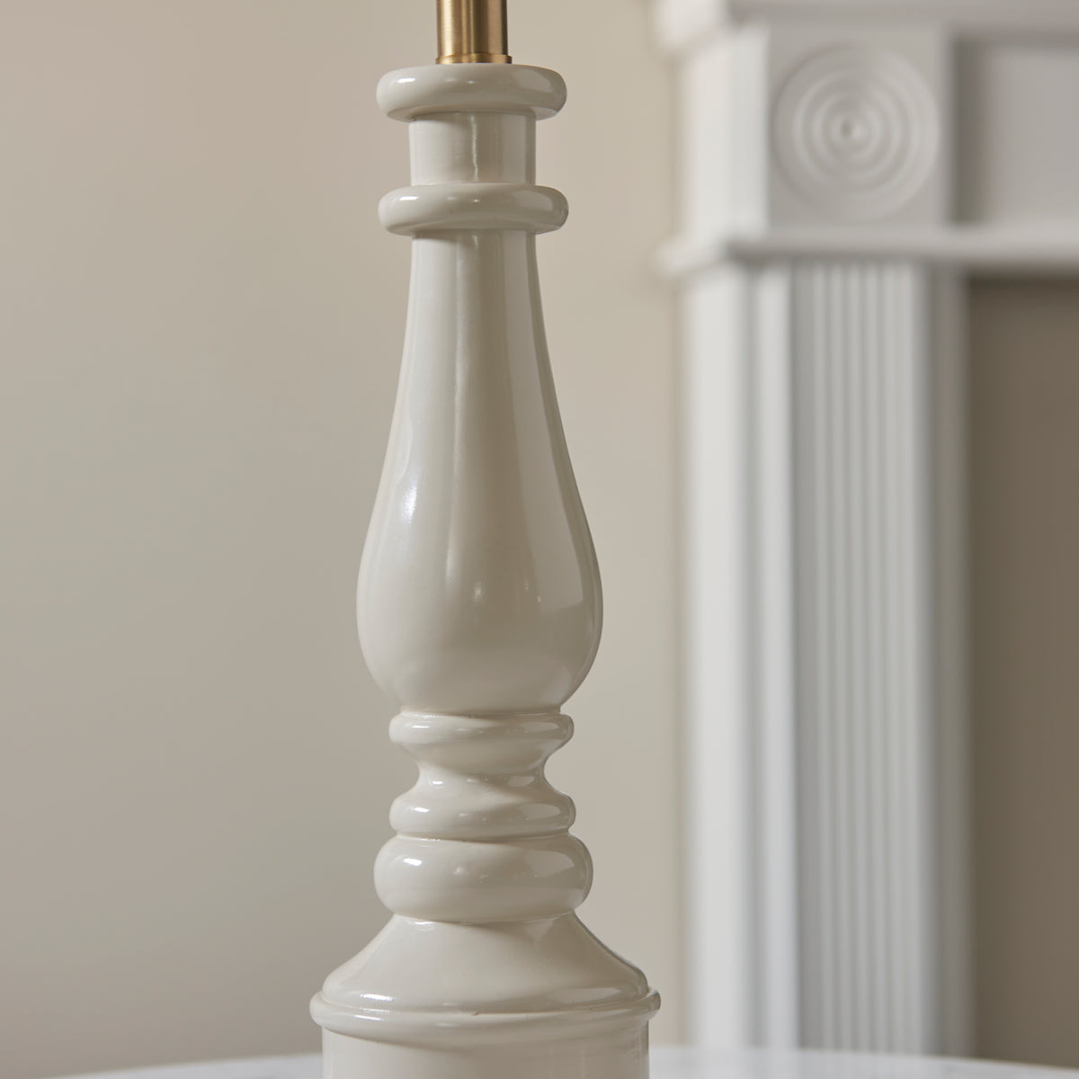 Close up of the gloss almond white turned spindle column of the Endon Myrtle table lamp, unlit, white fireplace surround in the background