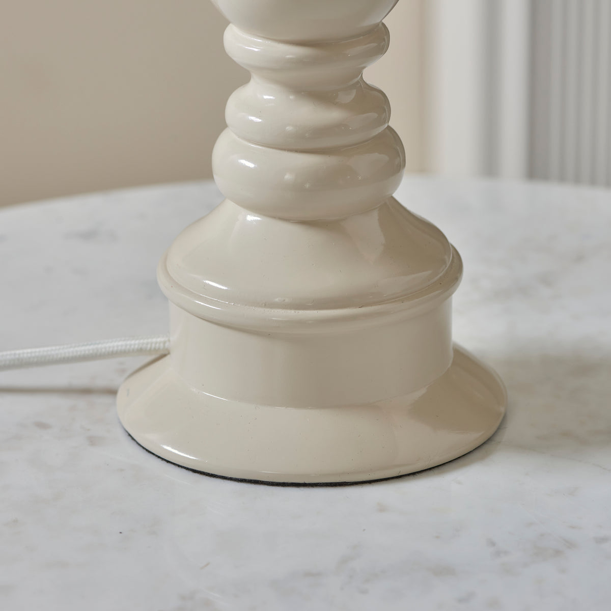 Close up of the Endon Myrtle table lamp foot in gloss almond white resin on a white marble table, white braided cable at the base