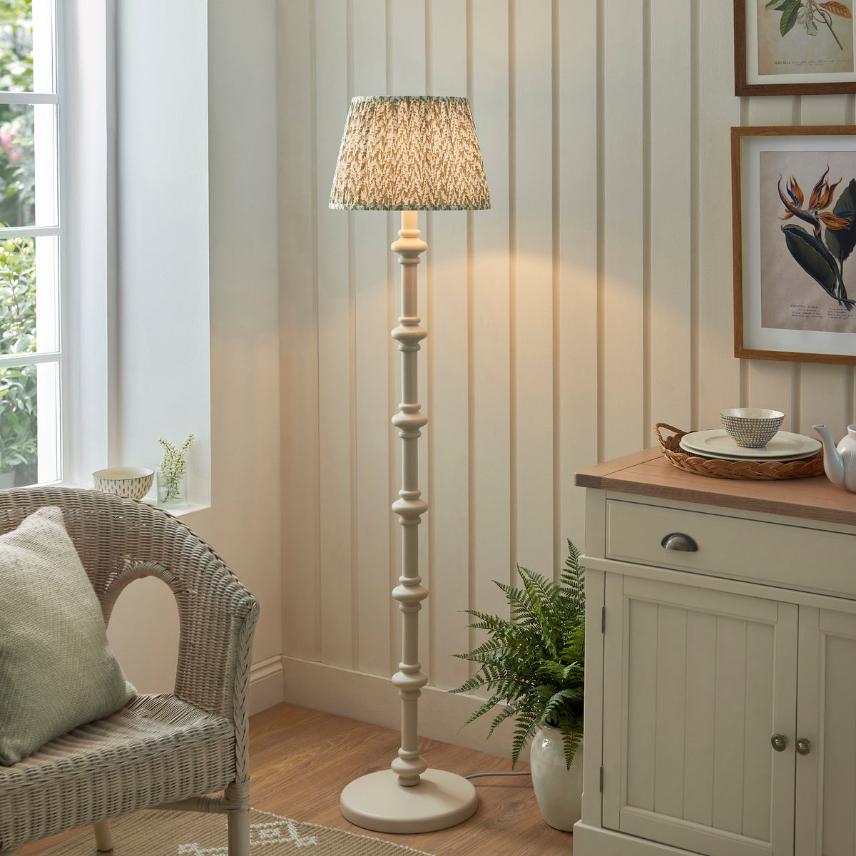 Endon Carnaby floor lamp lit in a cottage sitting room with painted panelling, rattan armchair, fern and sideboard, almond white stem, green Leaf shade