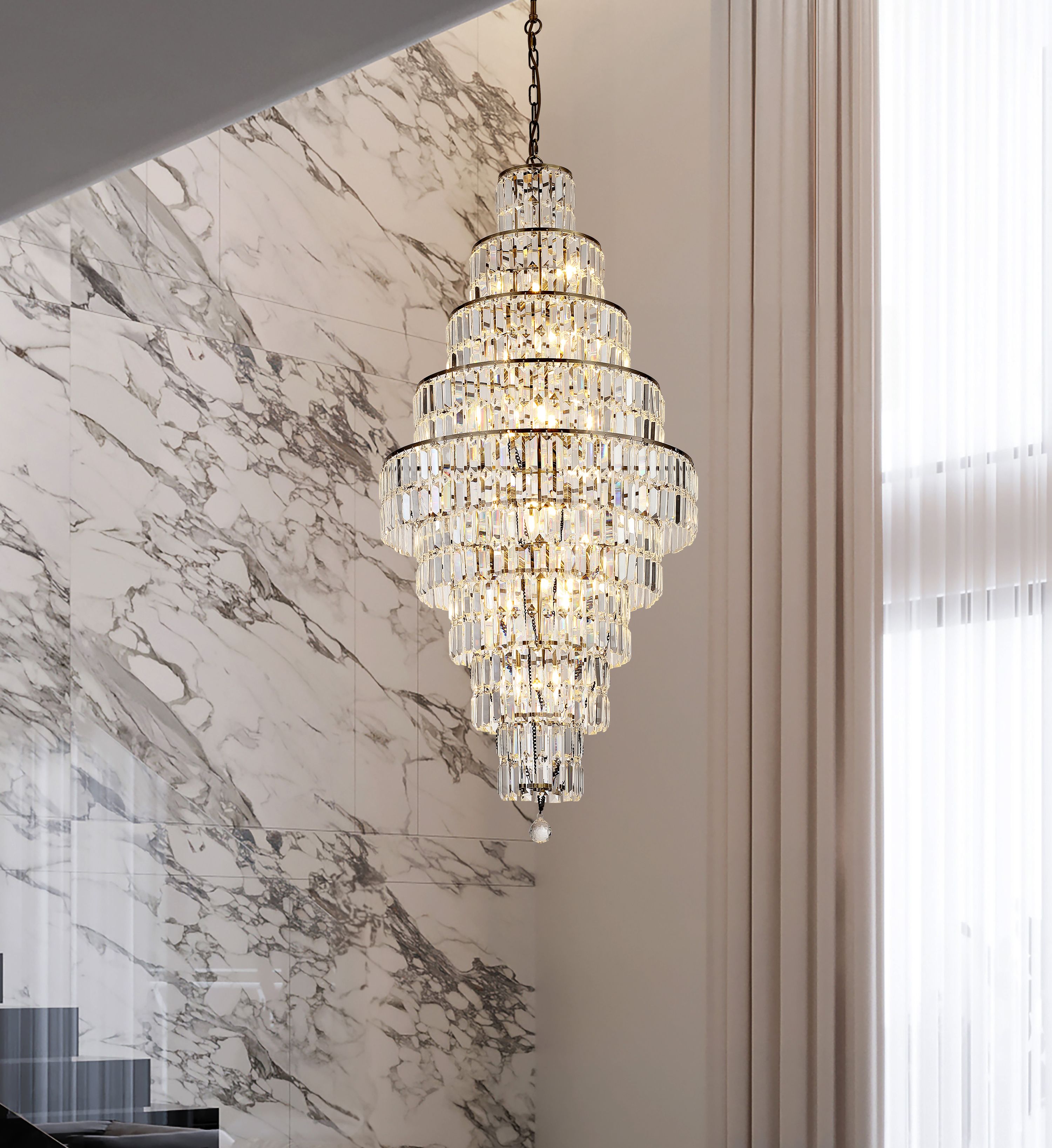 Searchlight Empire 13 light chandelier in antique brass and clear glass hanging in a stairwell beside a marble clad wall