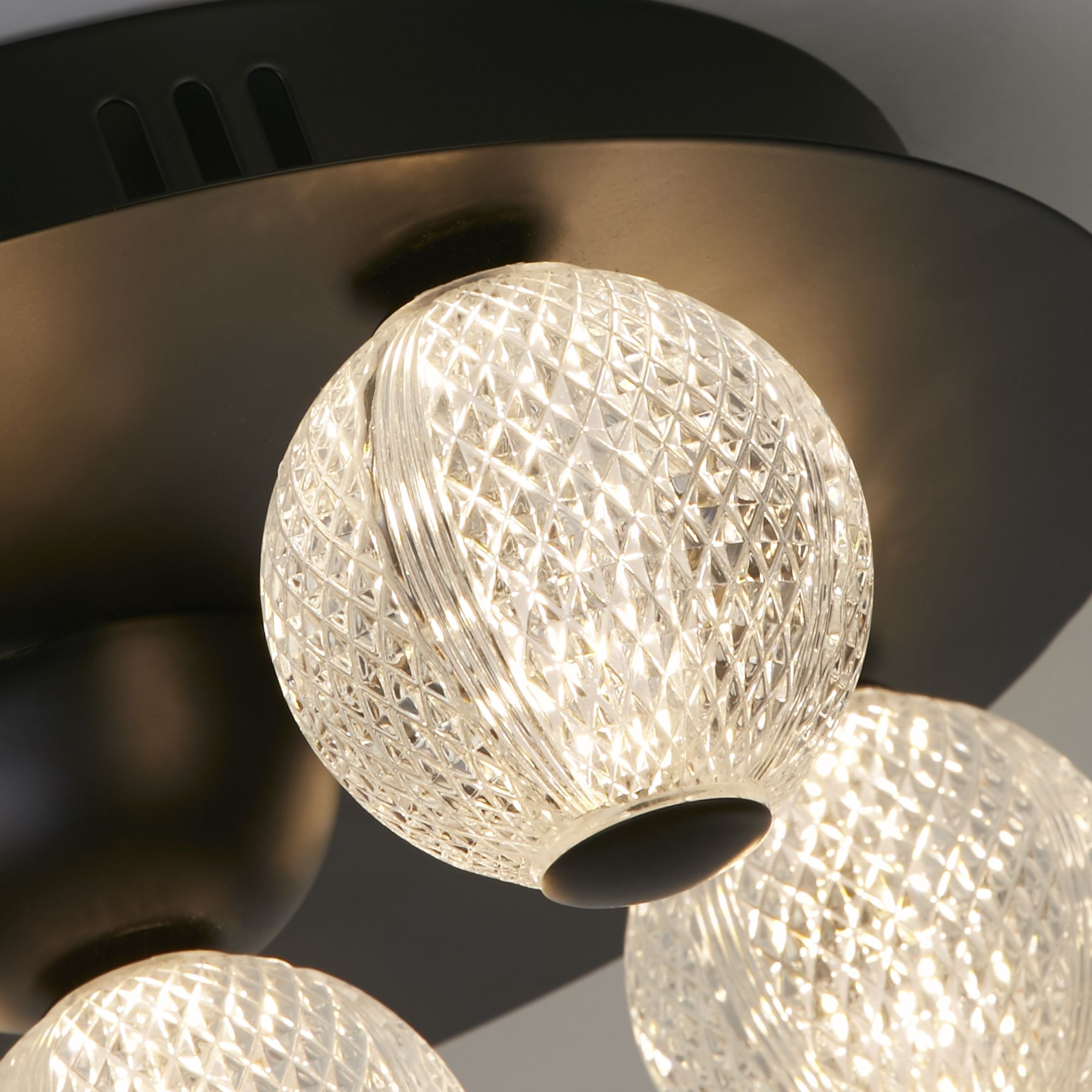 Close up of one textured glass sphere on the Asteroid flush ceiling light, showing the cut pattern lit from inside
