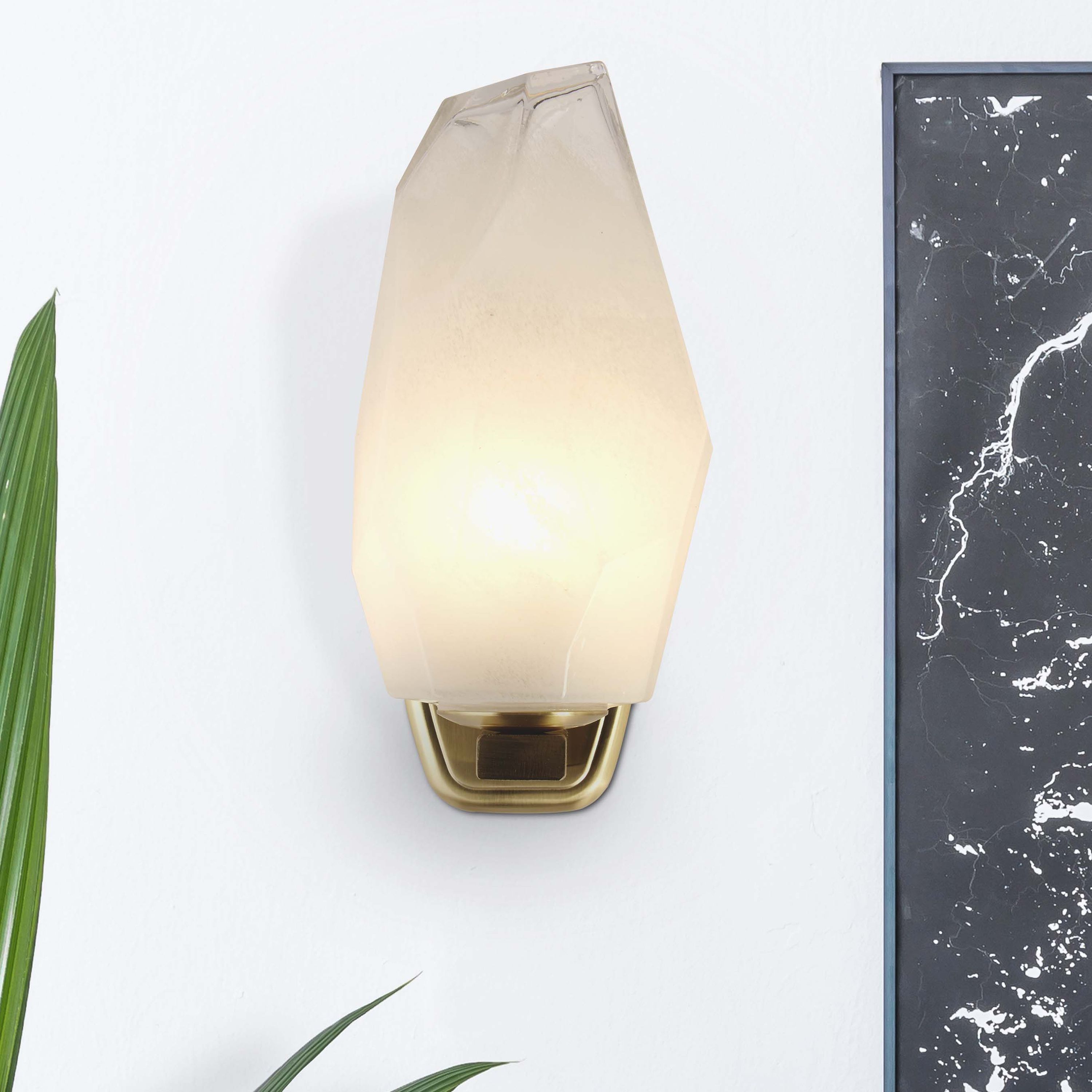 Rocky wall light mounted on a plain wall beside a potted plant and a dark marble framed panel, shade lit
