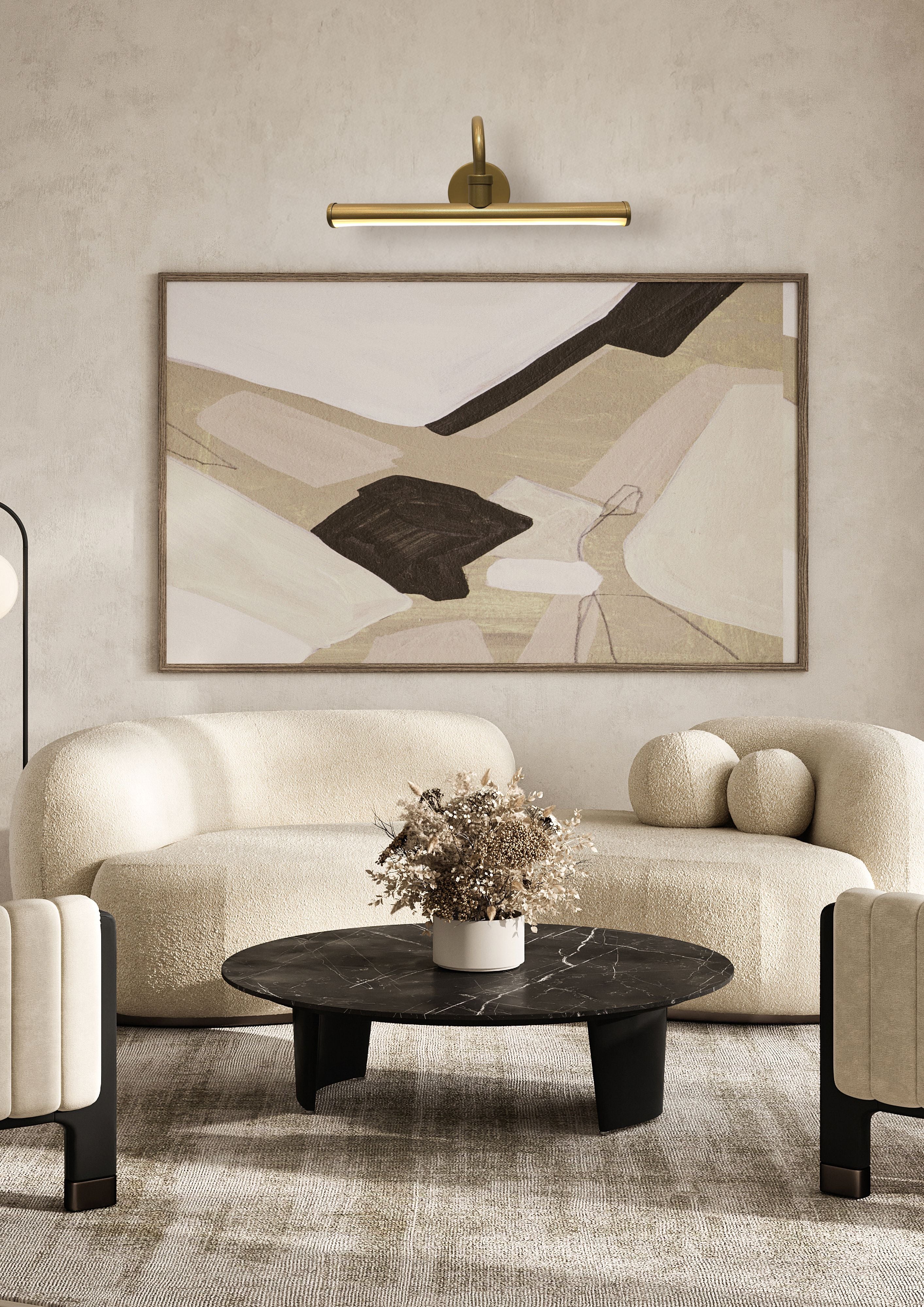 Vigo gold picture light styled above an abstract framed artwork in a beige living room with a boucle sofa and marble coffee table