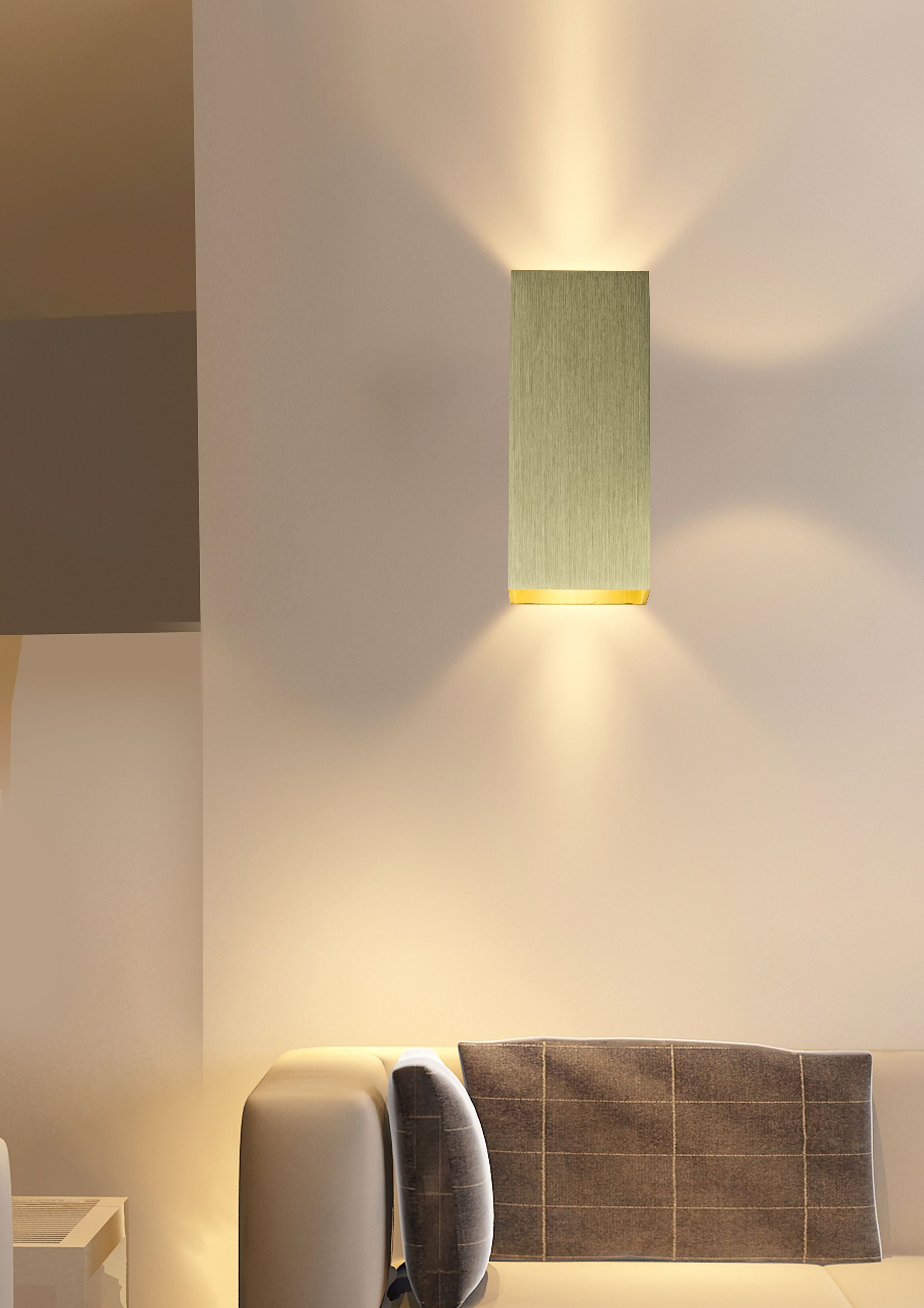 Searchlight Don wall light in brushed gold installed on a wall above a sofa, lit and casting light both upward and downward