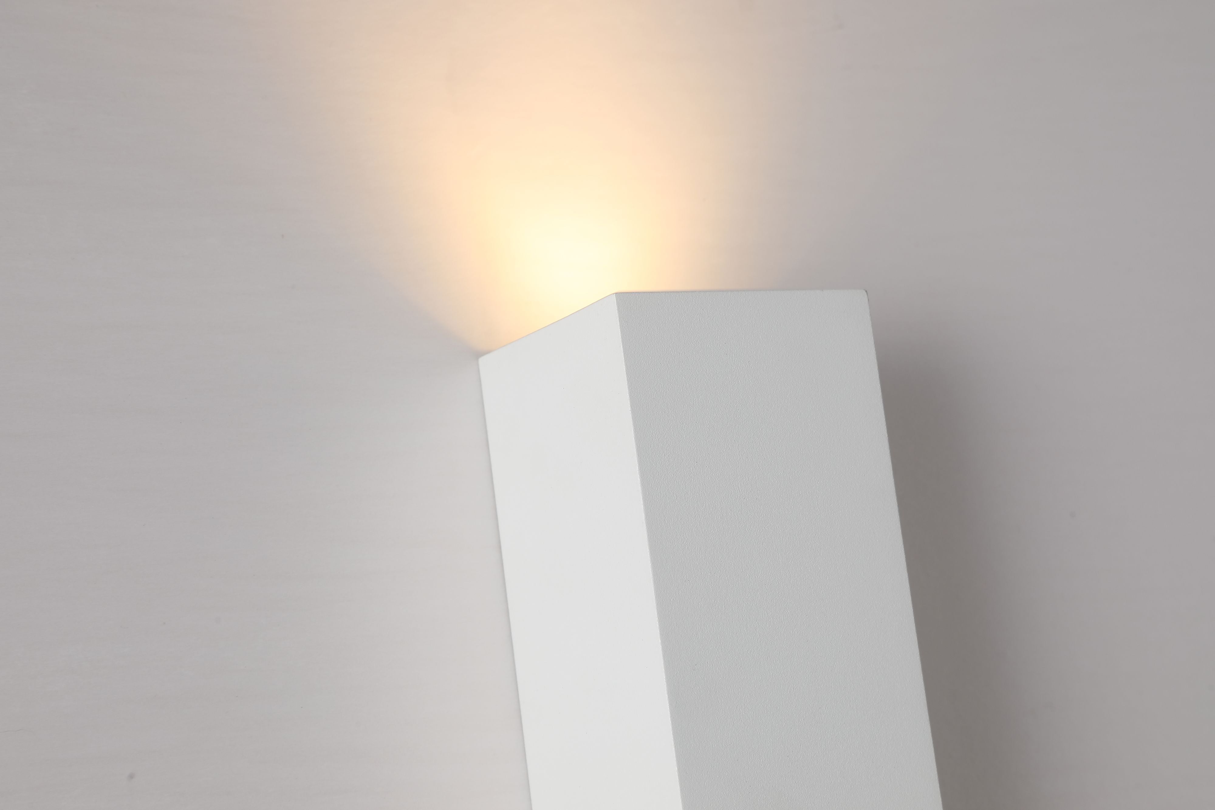 Close up of the Searchlight Don wall light in matte white showing the top corner with warm light spilling upward