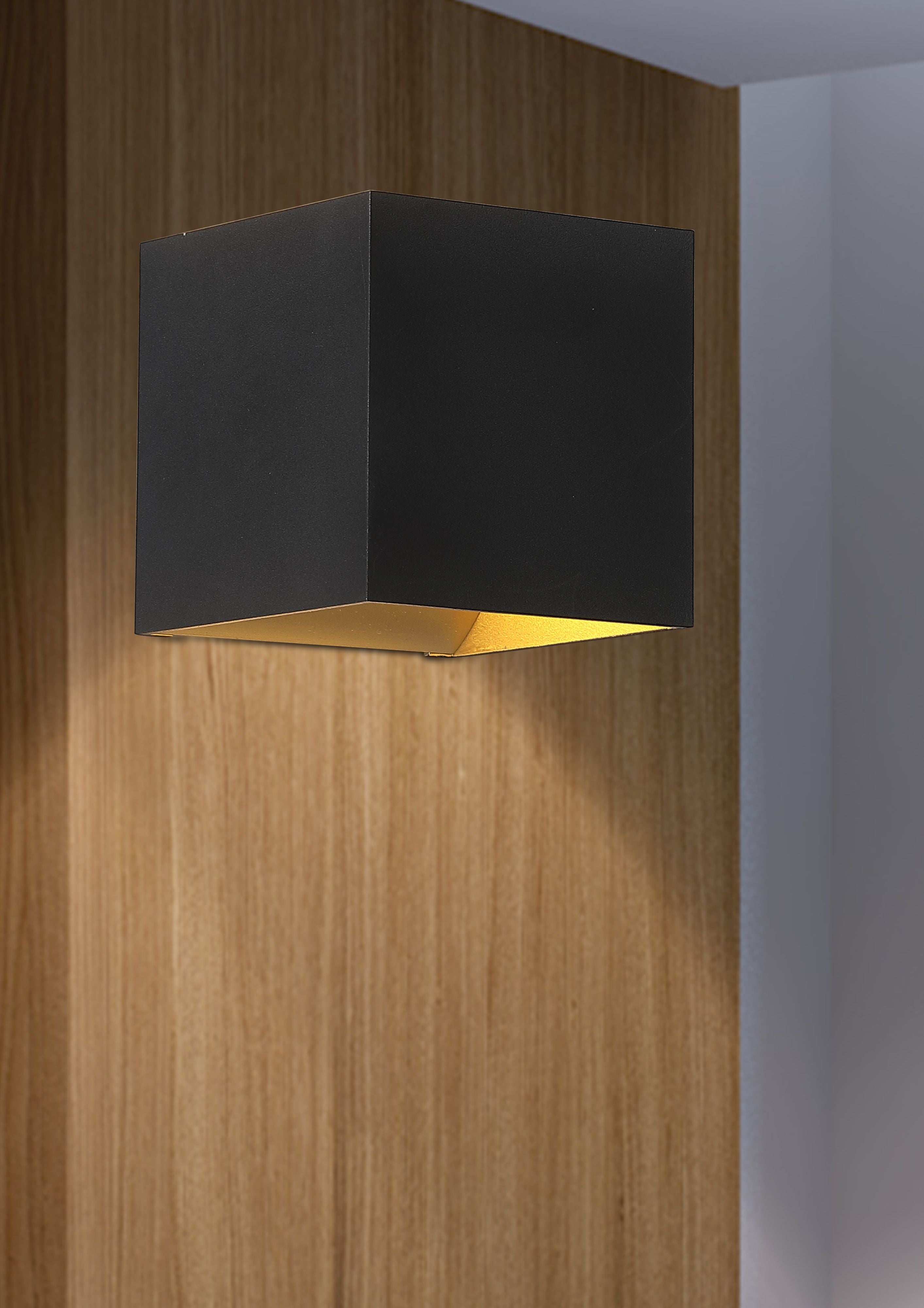 Searchlight Newton wall light in matte black with gold interior installed on a wood panelled wall, lit and casting light both upward and downward