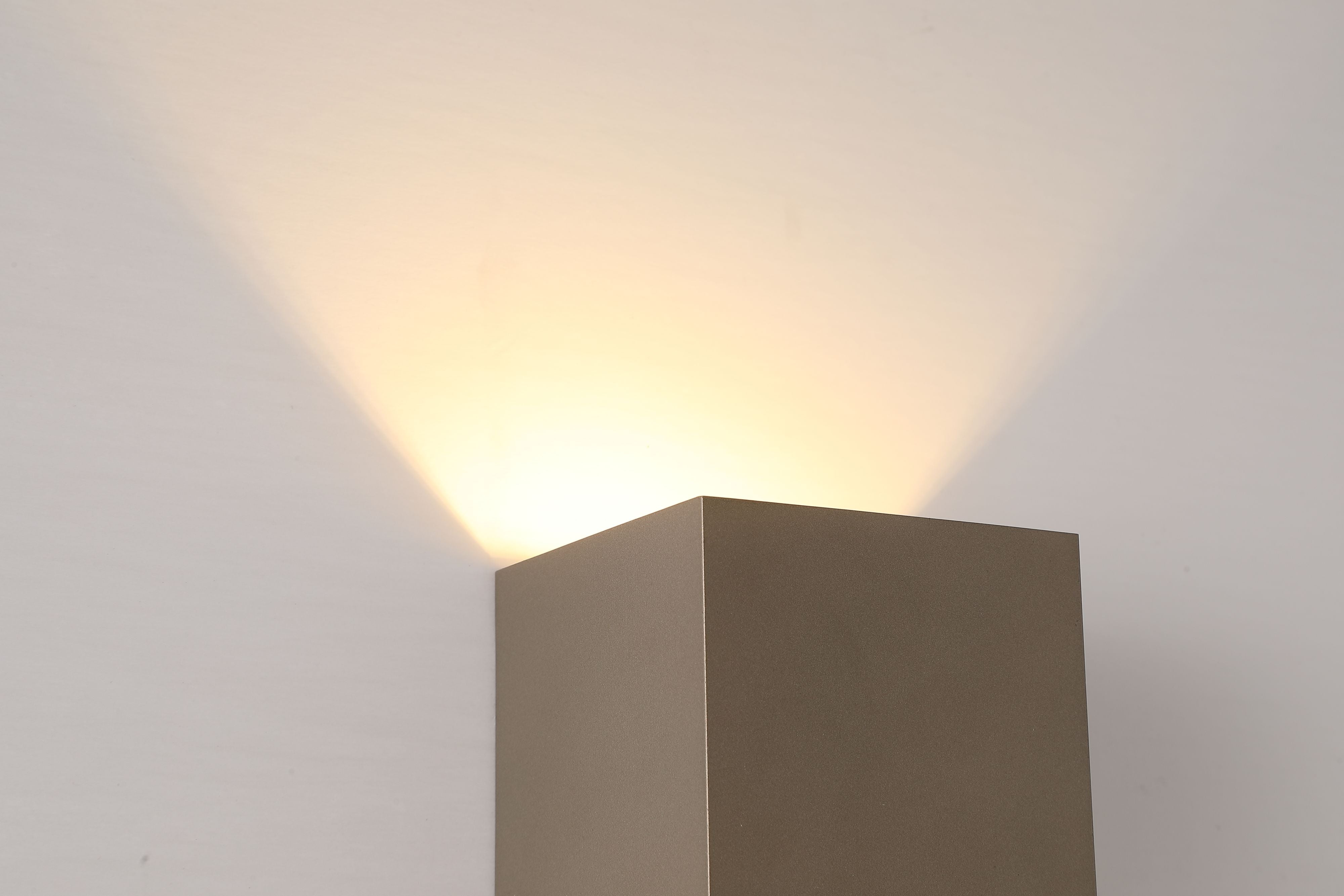 Close up of the top edge of the Newton Square wall light in latte, showing warm light spilling upward from the fitting