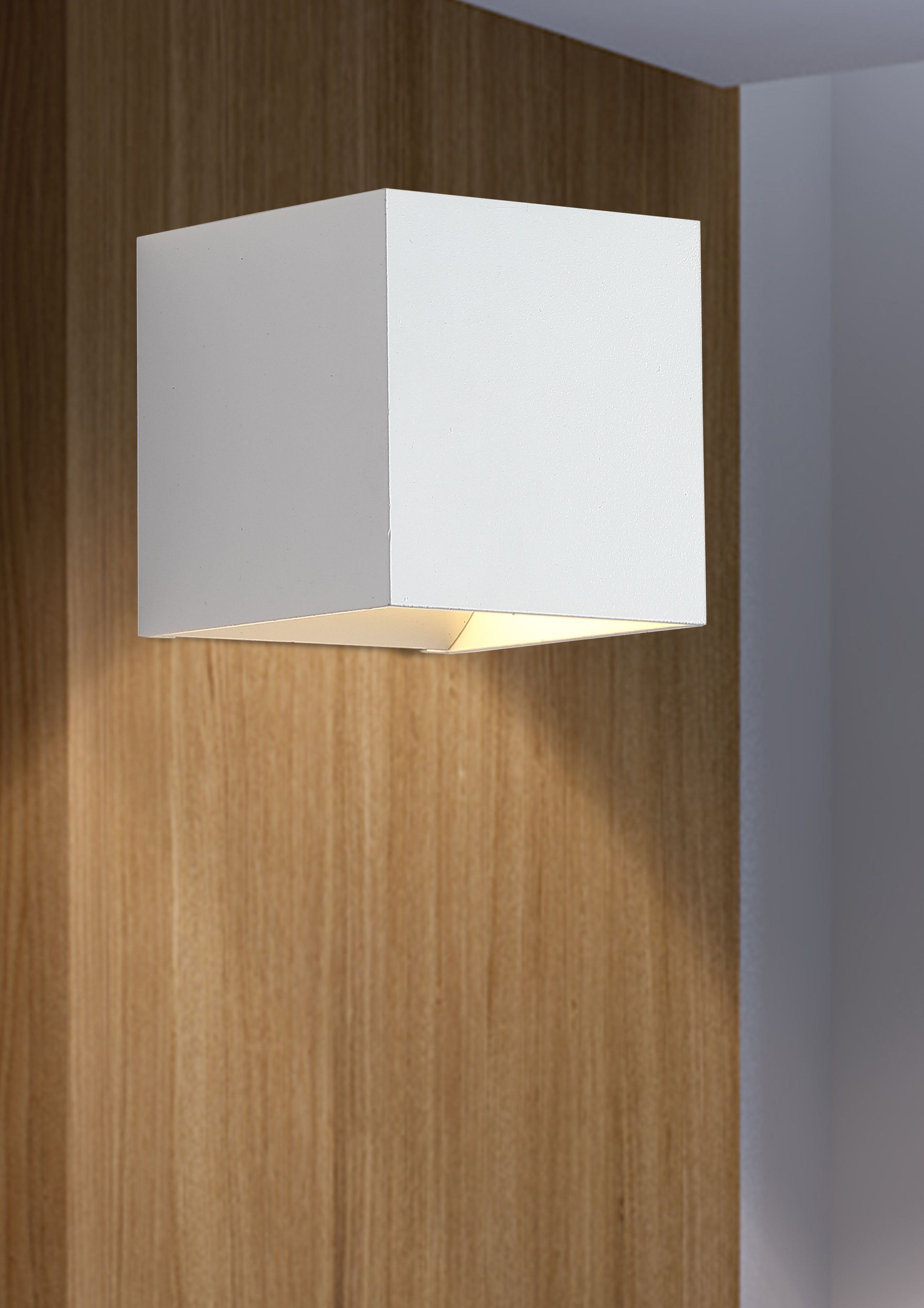 Newton Square Up & Down Wall Light in sand white installed on a wood panelled wall, glowing with warm light above and below the fitting