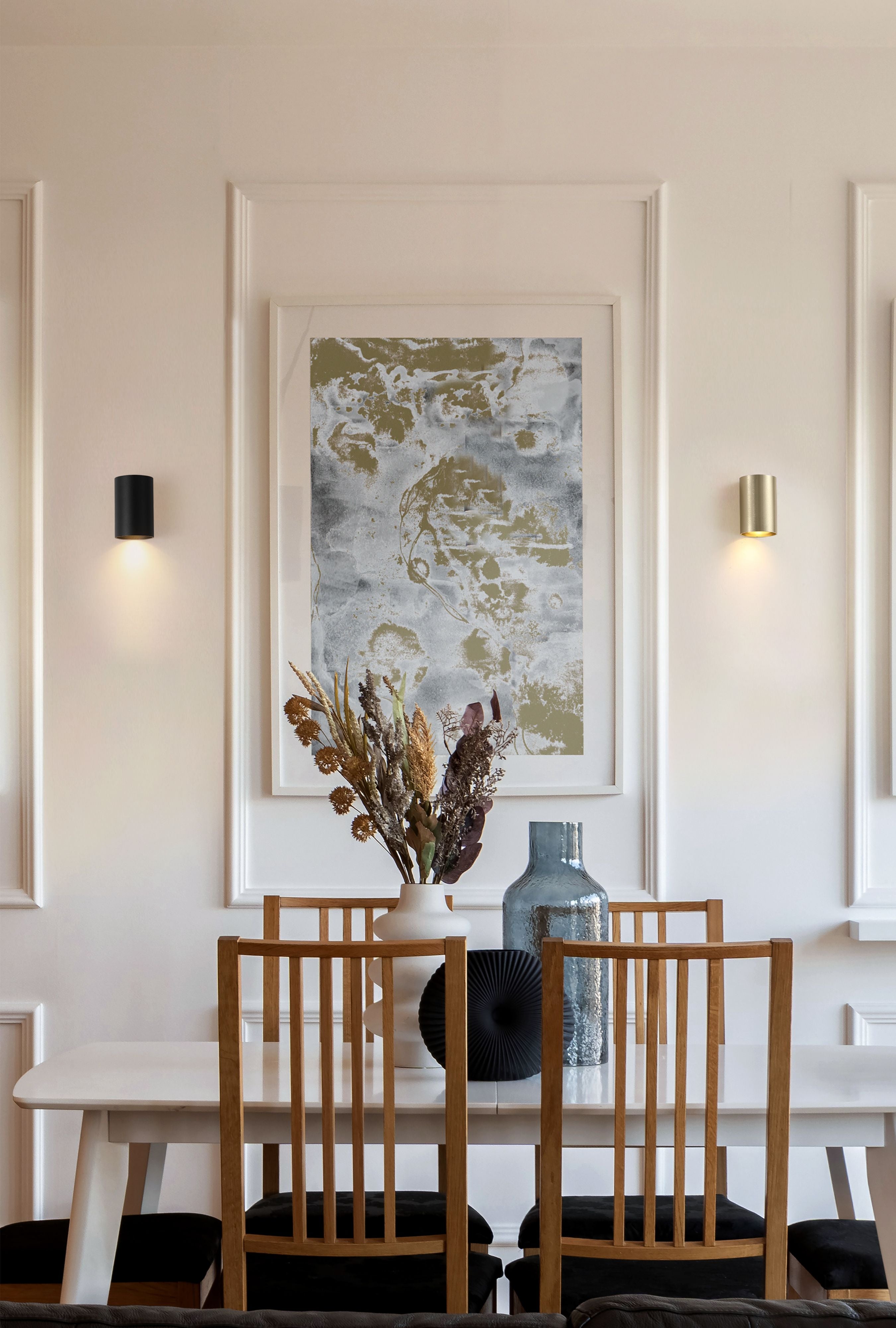 Searchlight Cyls Cylinder Down Wall Light shown in a styled dining room, gold finish on the right wall and black finish on the left wall either side of a framed artwork, both lit