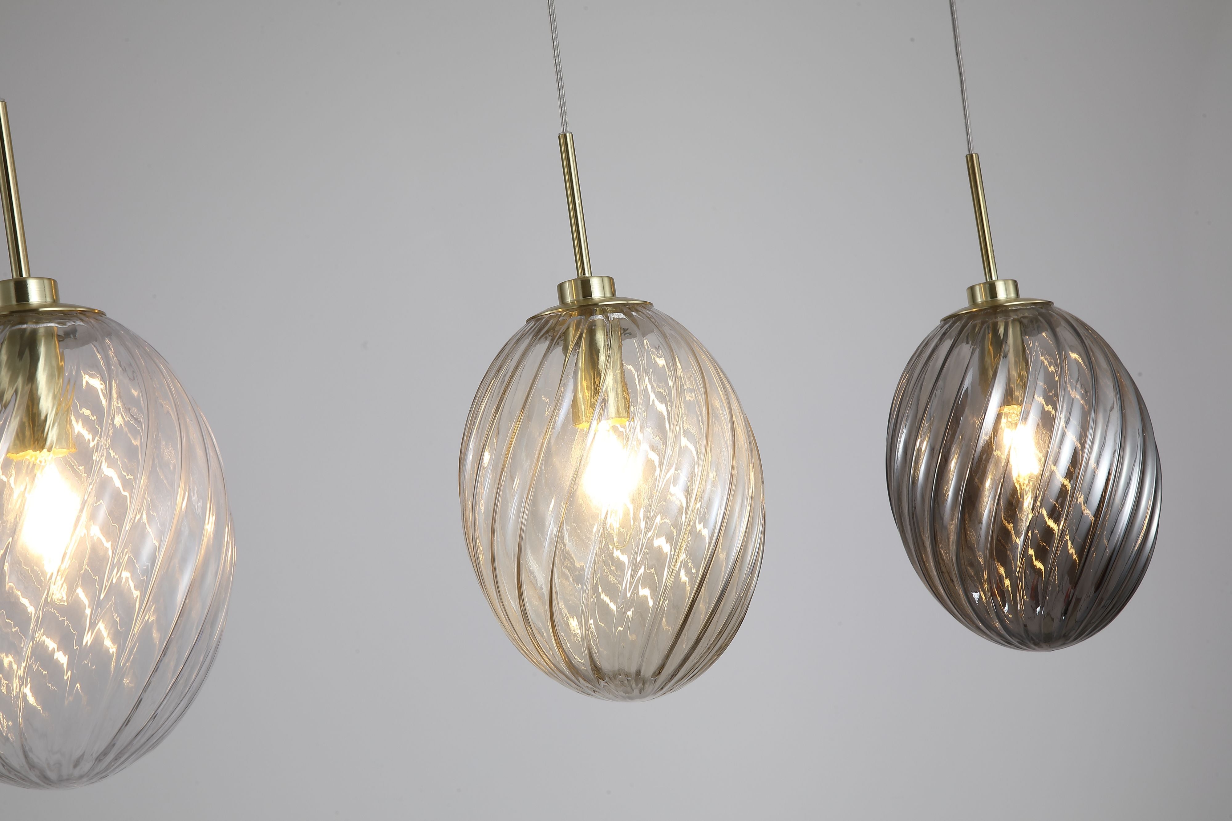 Close up of the three swirled glass shades on the Searchlight Whirl bar pendant in clear, champagne and smoked tones, showing the ribbed texture and satin brass fittings