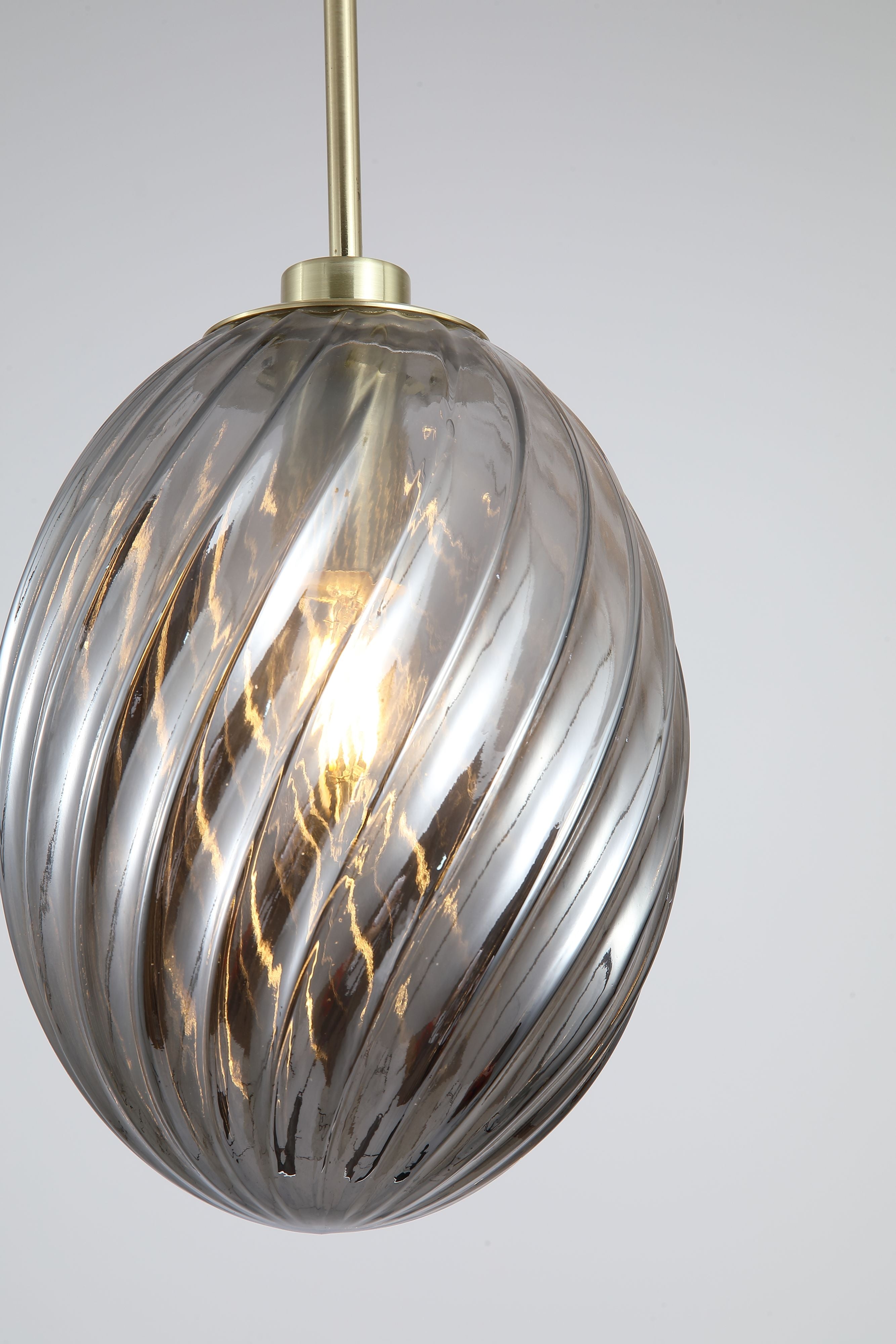 Close up of the smoked grey swirled glass shade on the Searchlight Whirl pendant, showing the ribbed spiral texture, satin brass gallery and lit bulb inside