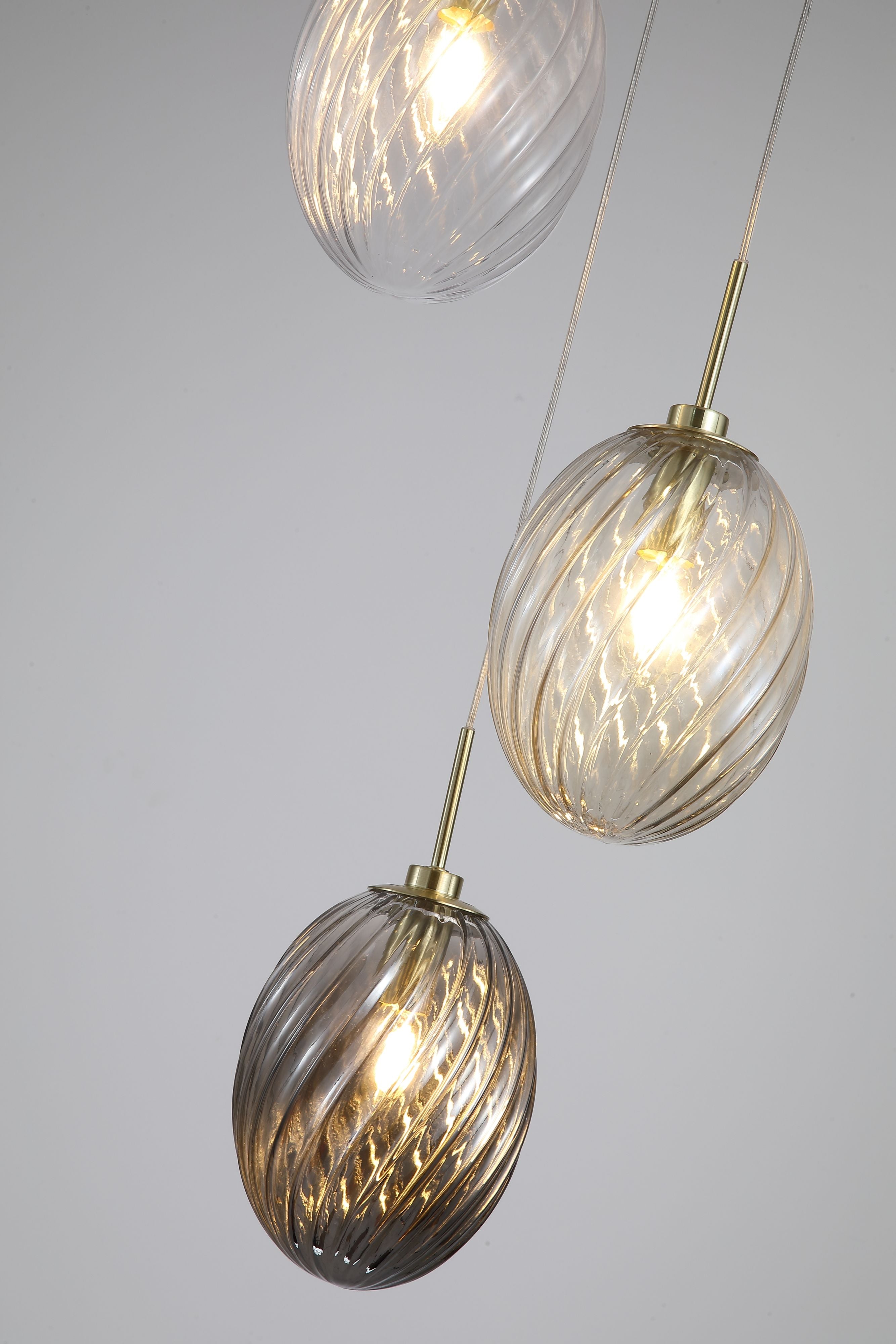 Close up of all three swirled glass shades on the Searchlight Whirl multi drop pendant in clear, champagne and smoked tones, cascading at staggered heights against a soft grey background