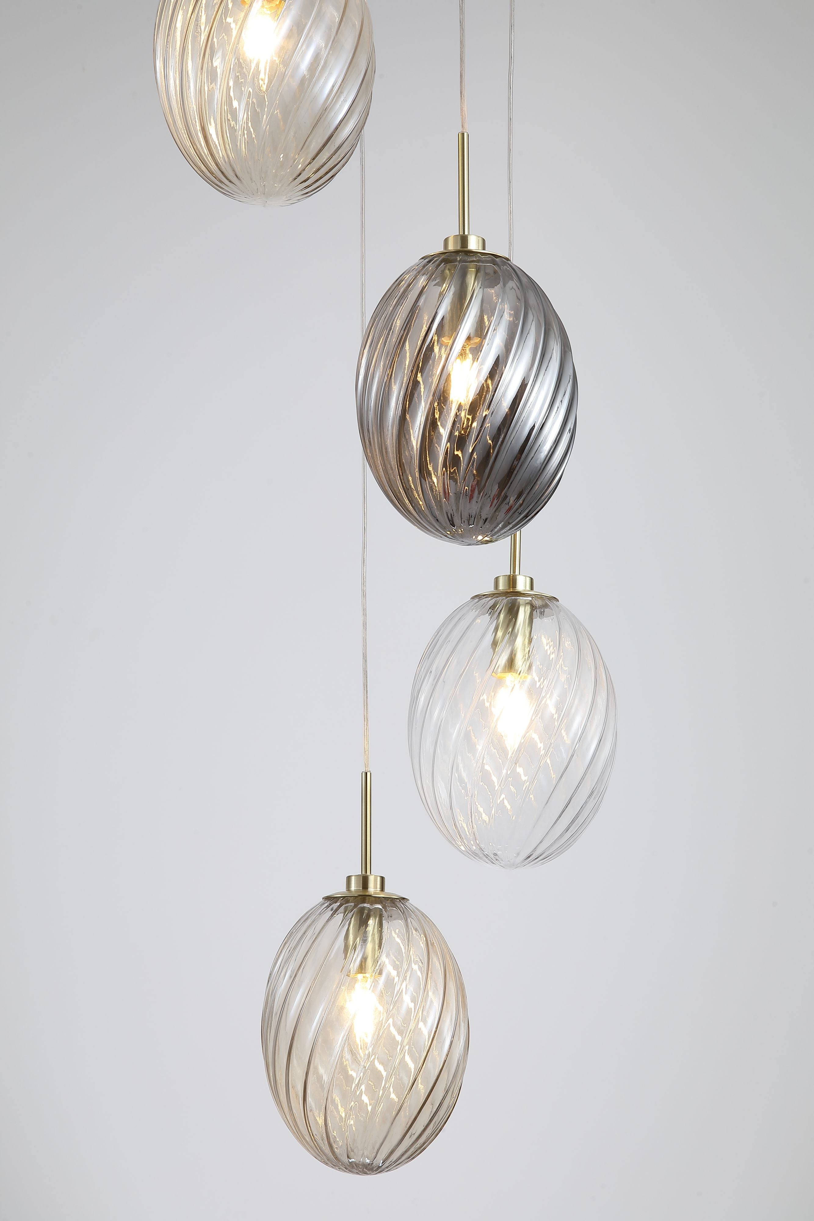 Close up of the swirled glass shades on the Searchlight Whirl 5 light multi drop pendant including the smoked and clear tones, showing the ribbed texture and satin brass fittings against a soft grey background