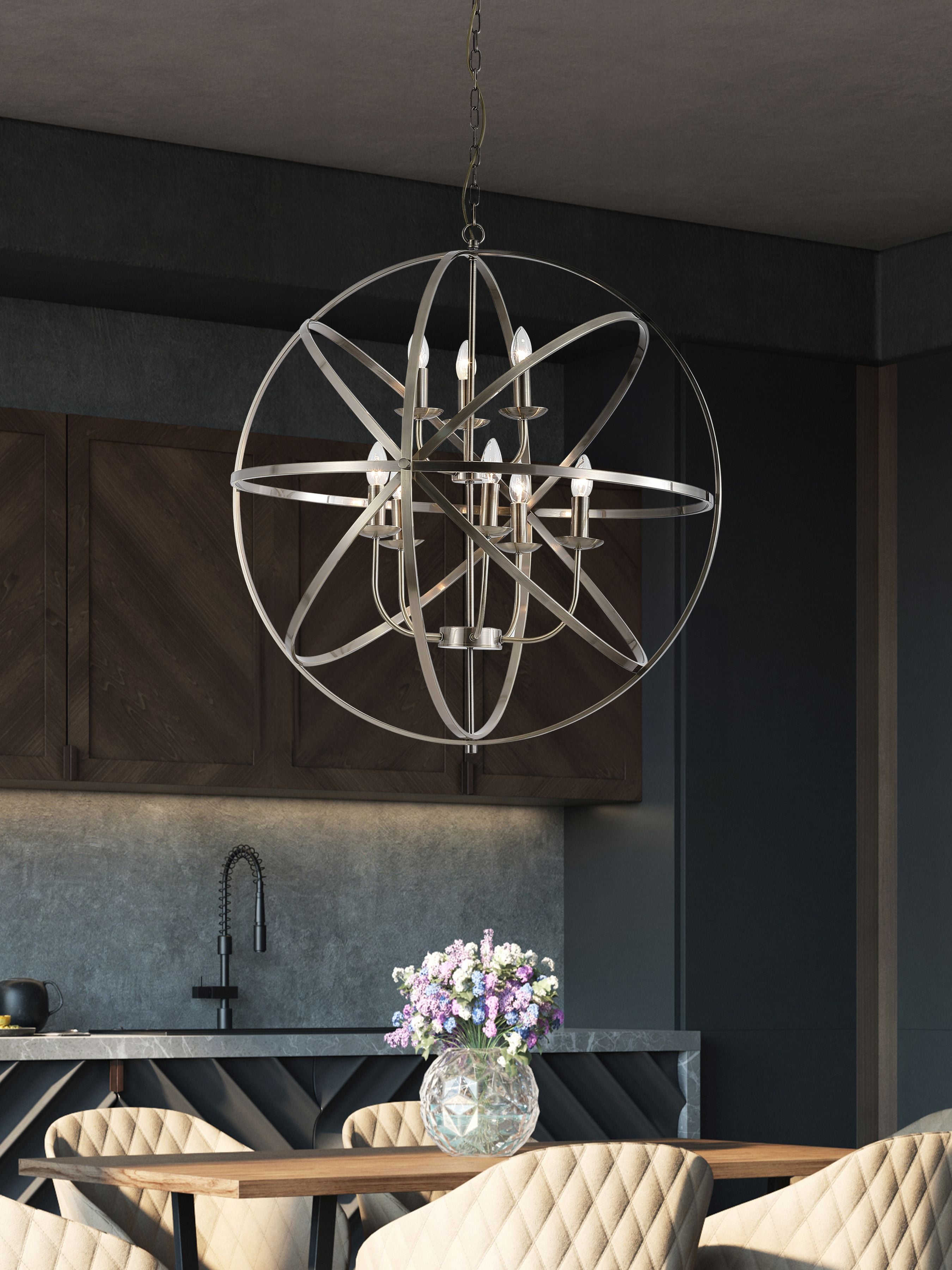 Orbit pendant in antique brass hanging above a dining table in a dark modern kitchen with a floral centrepiece