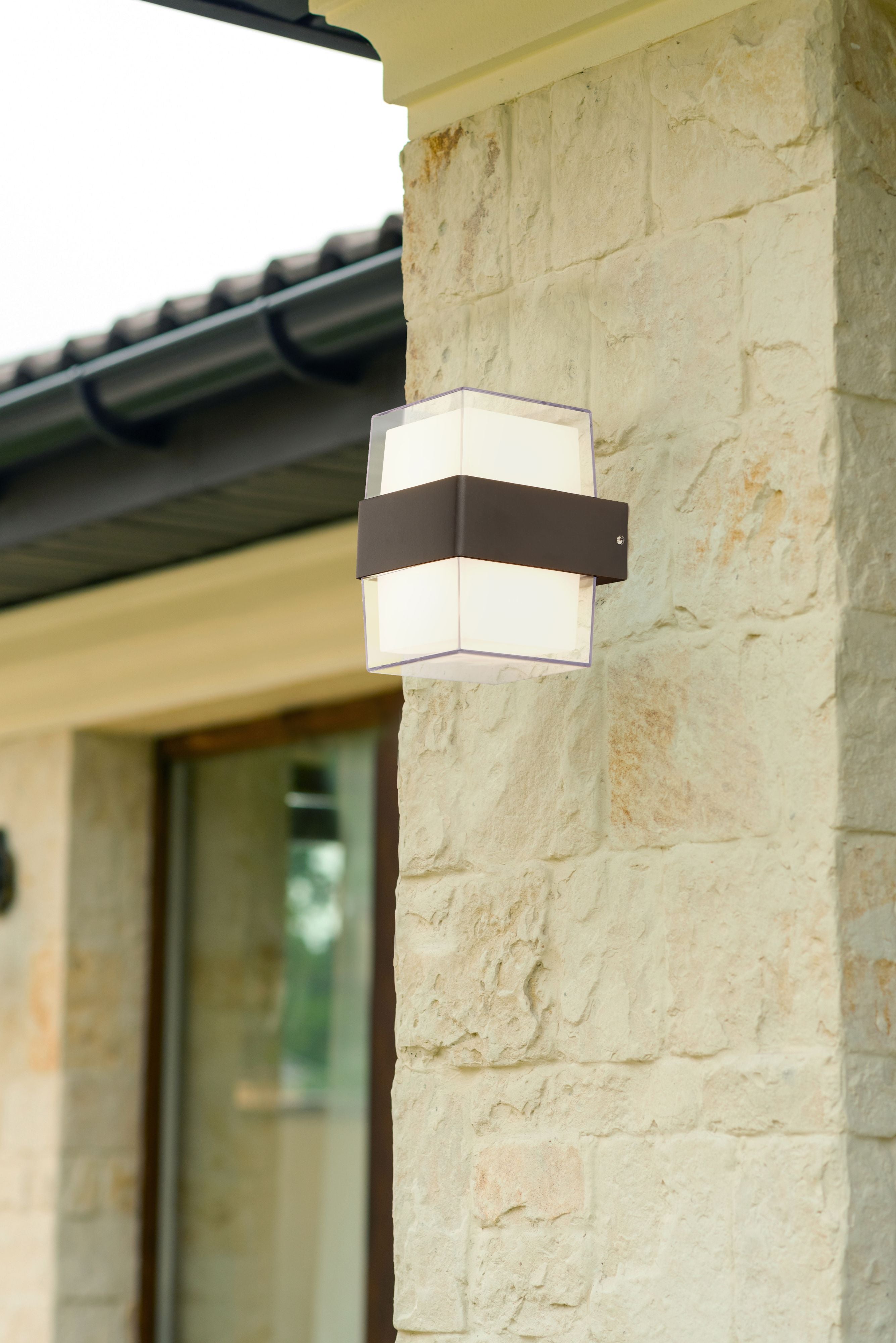 Searchlight Pittsburgh square outdoor wall light installed on a stone wall pillar beside a glazed door, lit warm white above and below the black band
