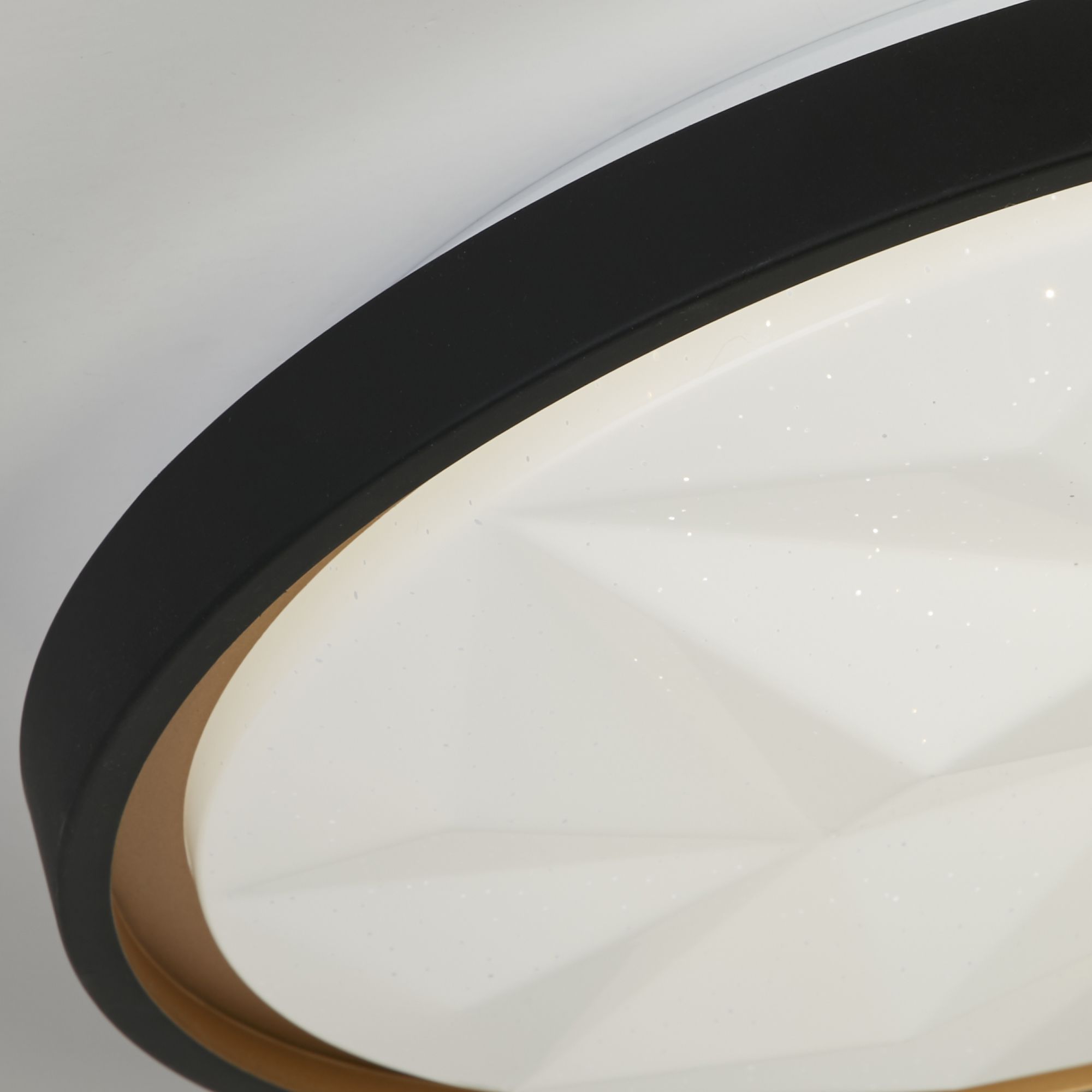 Close up of the Satellite flush light's black rim and gold inner trim around the faceted acrylic diffuser