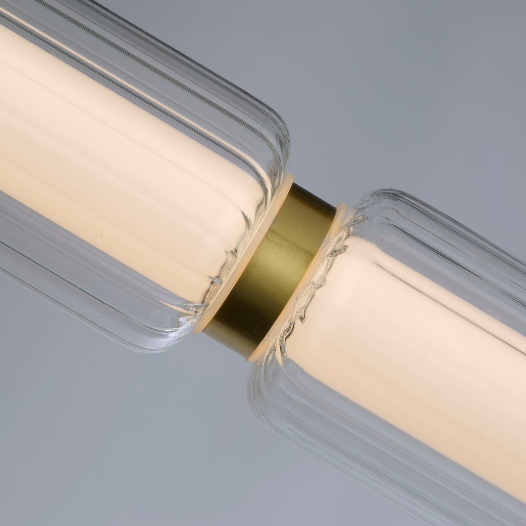 Close up of the Searchlight Mod LED Pendant showing the satin brass ring joining two ribbed glass segments, lit from within