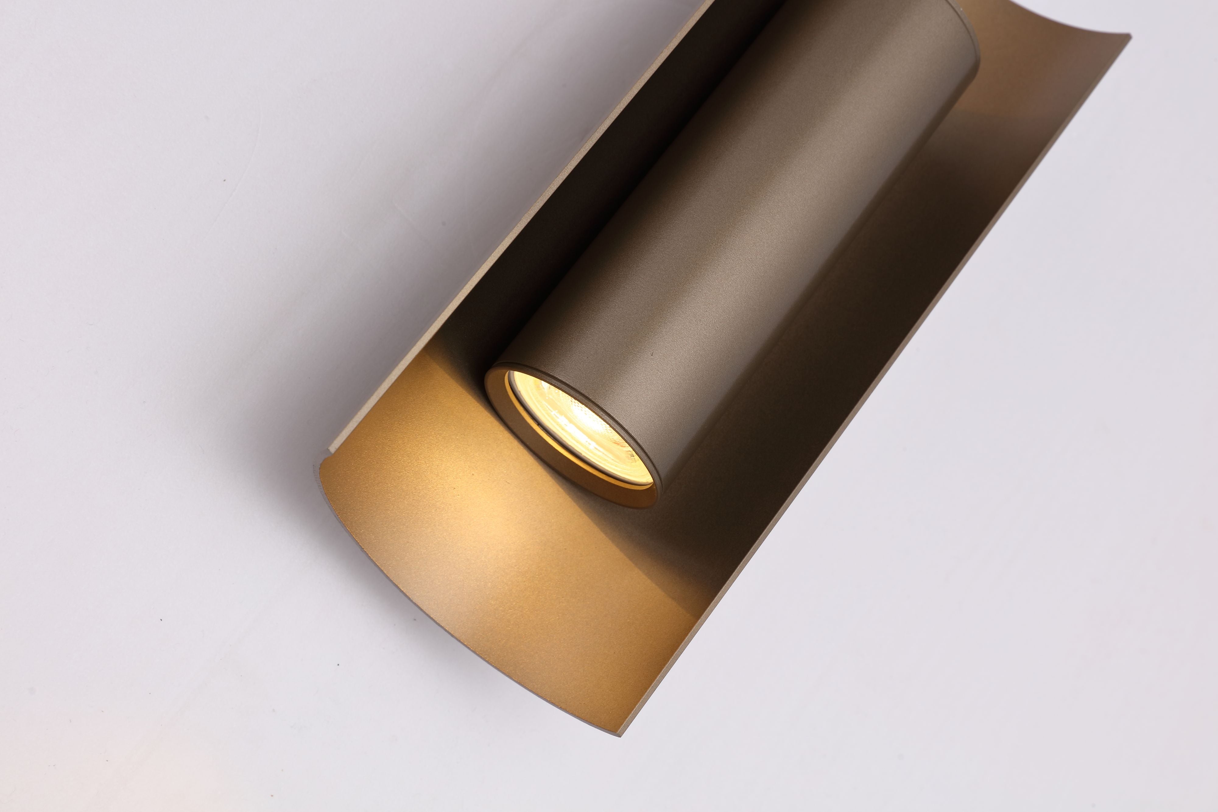 Close up angled detail of the Roll wall light's latte metal cylinder and GU10 bulb holder against the gold toned interior
