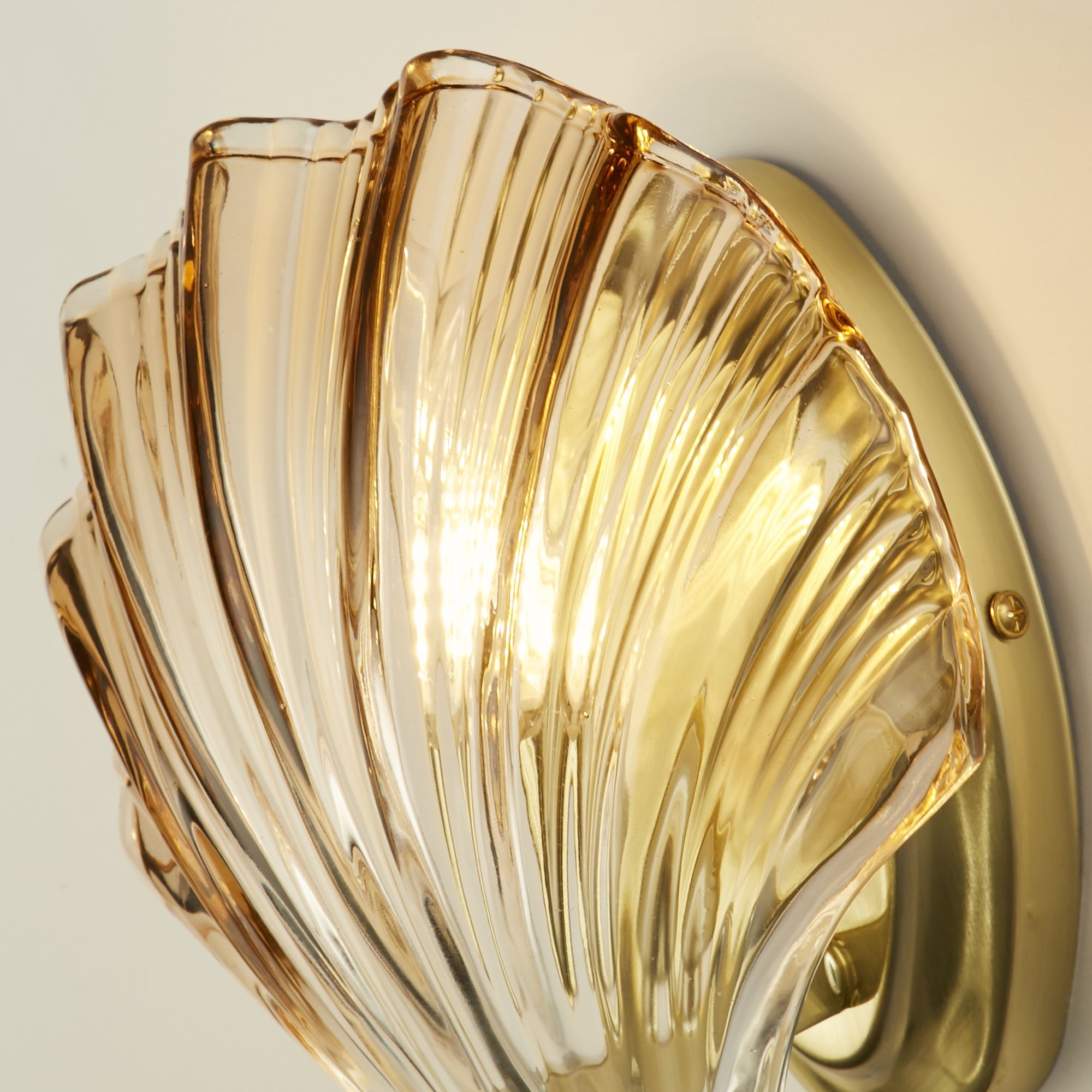Close up of the Shell's amber ombre glass shade showing the ribbed texture and satin brass wall plate