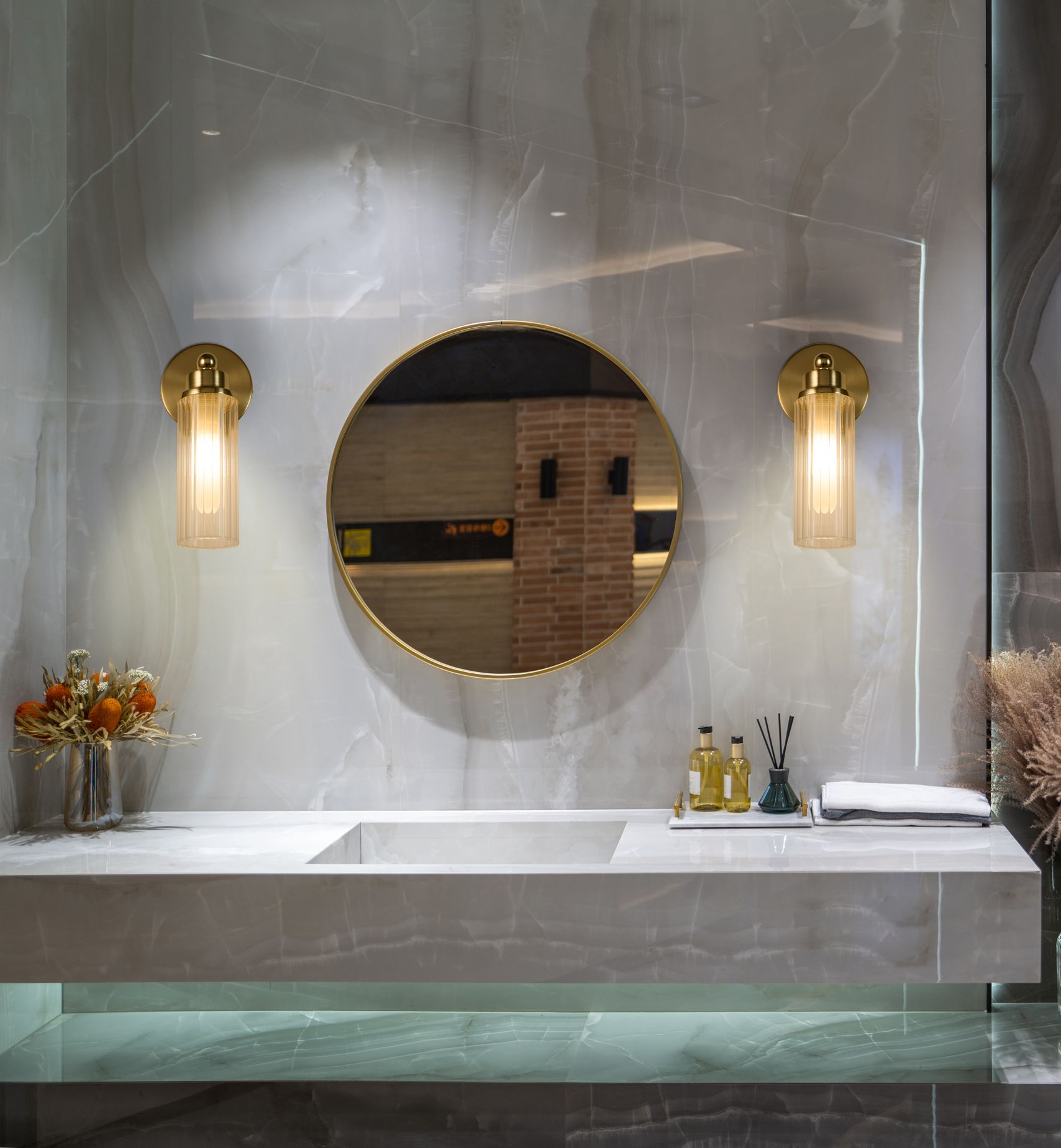 Searchlight Imperial 1 light wall light in satin brass mounted either side of a round mirror above a marble bathroom vanity