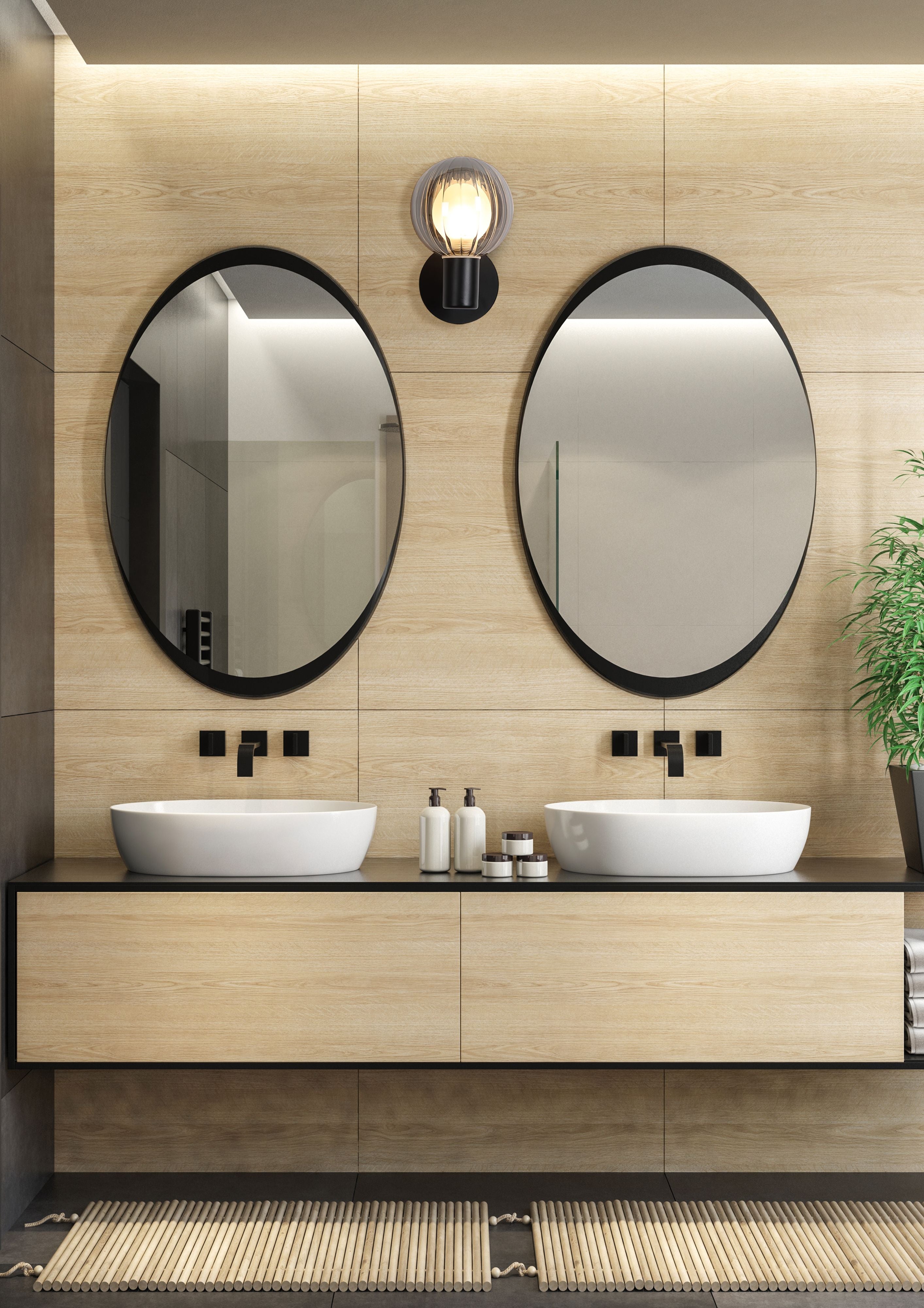 Luminsphere wall light mounted on a wood tiled wall between two black framed oval mirrors above twin countertop basins in a bathroom