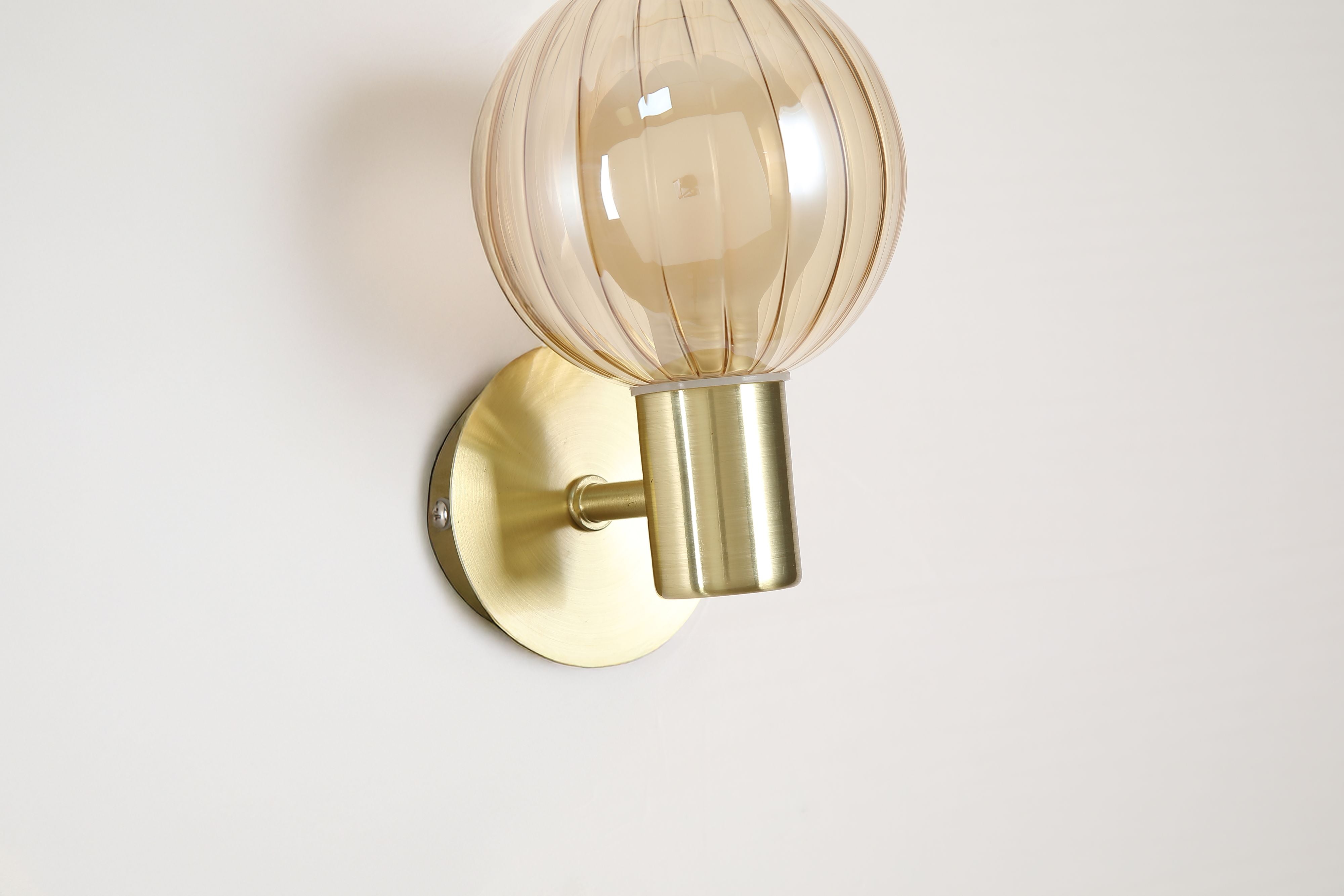 Close up of the ribbed champagne glass globe and brushed brass fitting on the Searchlight Luminsphere 1 Light Wall Light