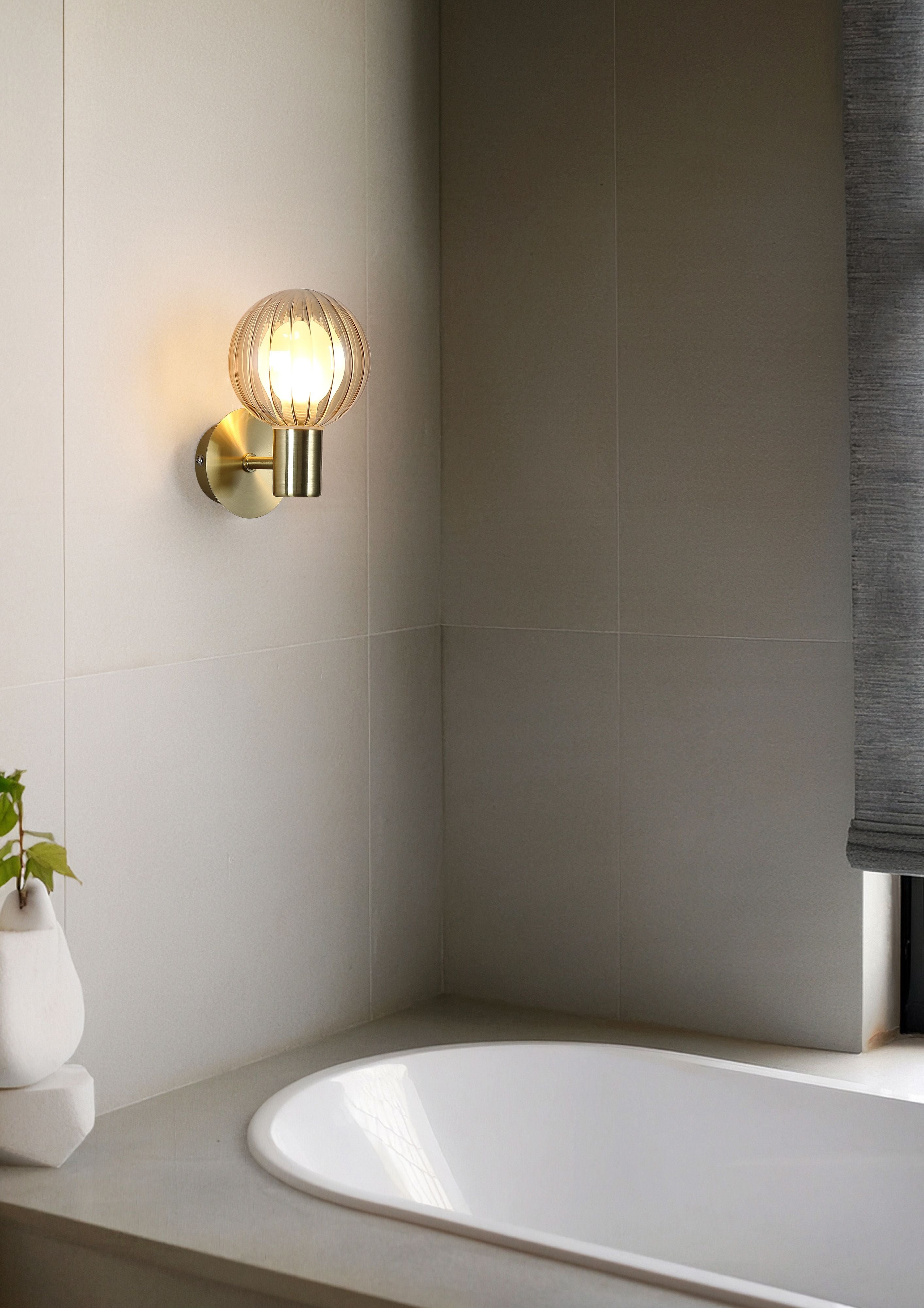 Searchlight Luminsphere 1 Light Wall Light in brass installed above a bathtub in a styled bathroom, glass globe lit