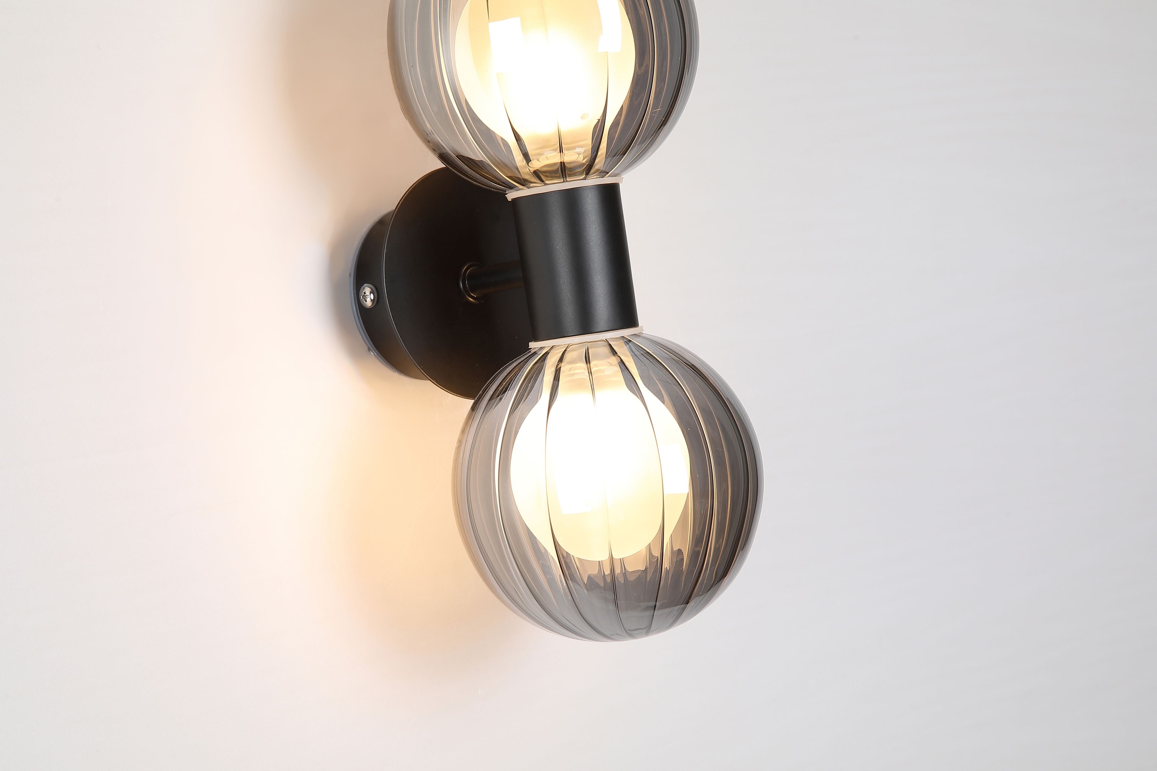 Close up of the smoked ribbed glass globes and matte black centre bracket on the Searchlight Luminsphere 2 Light Wall Light