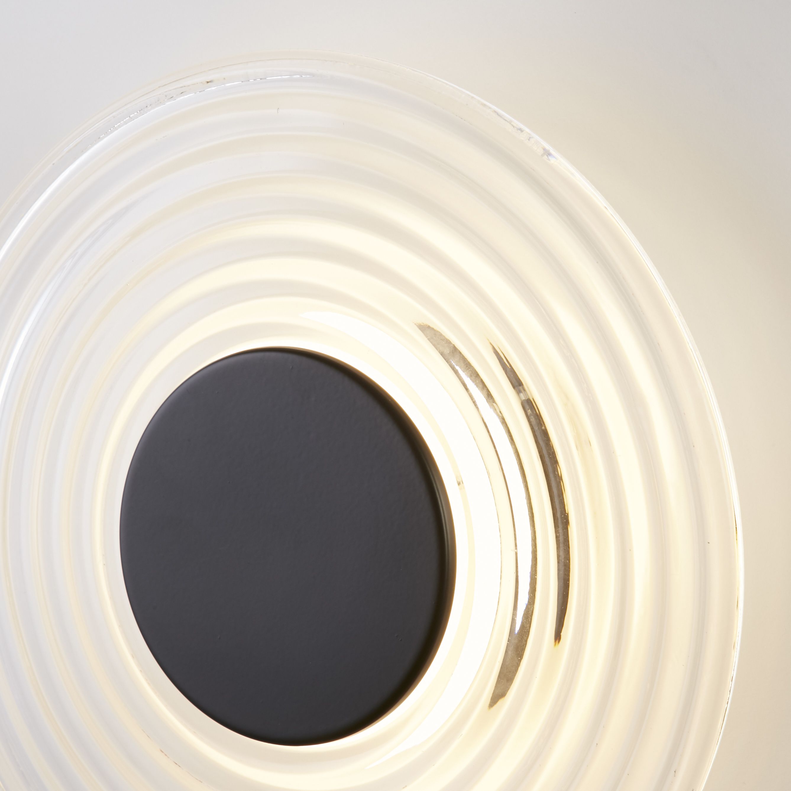 Close up detail of the Cleo wall light's matt black centre disc and ribbed clear glass shade