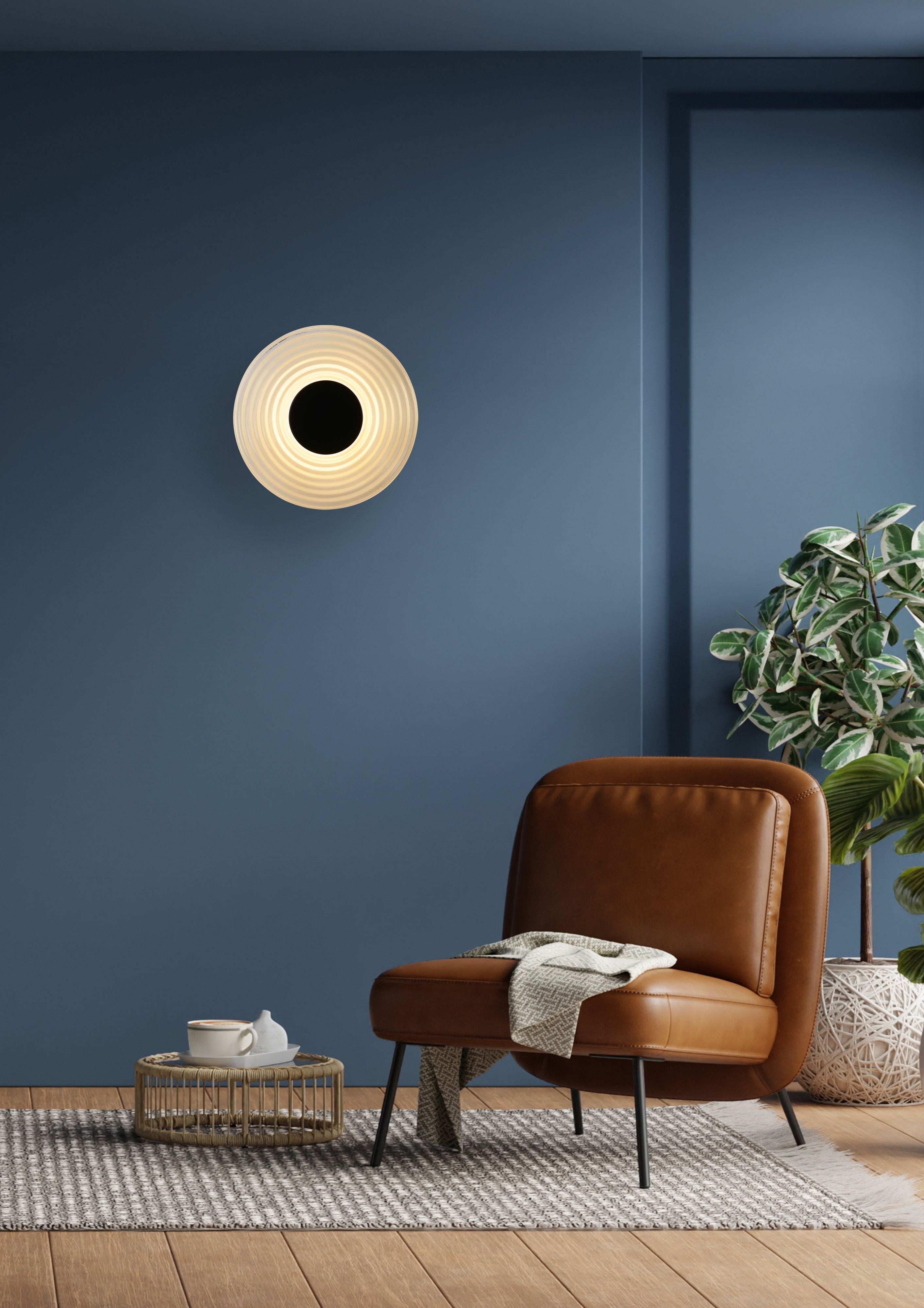 Dark blue living room with a leather armchair and side table, showing the Cleo wall light in matt black and clear glass lit and mounted above
