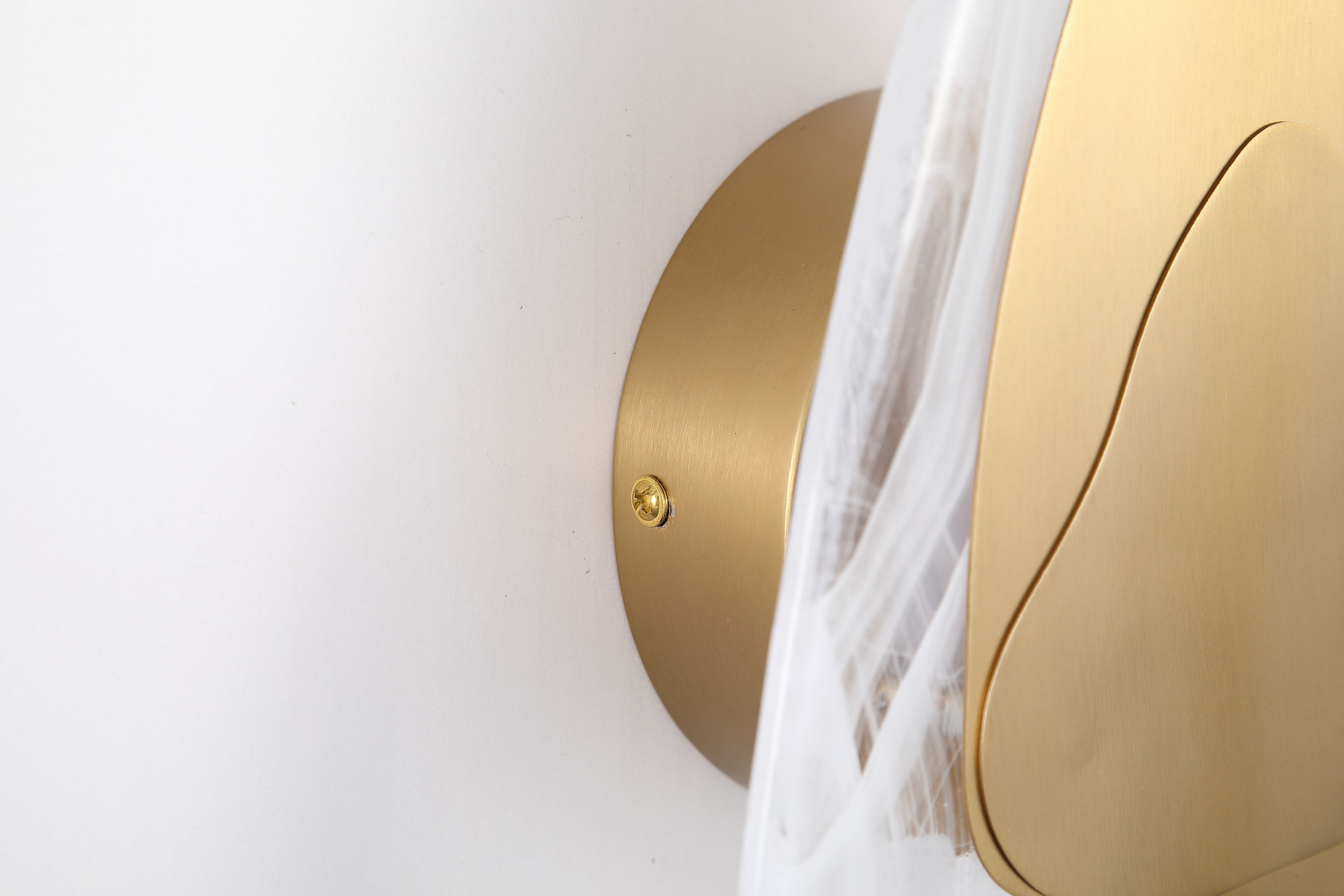 Close up of the Destiny wall light's brushed brass wall mounting plate and triangular accent plate against the textured glass shade