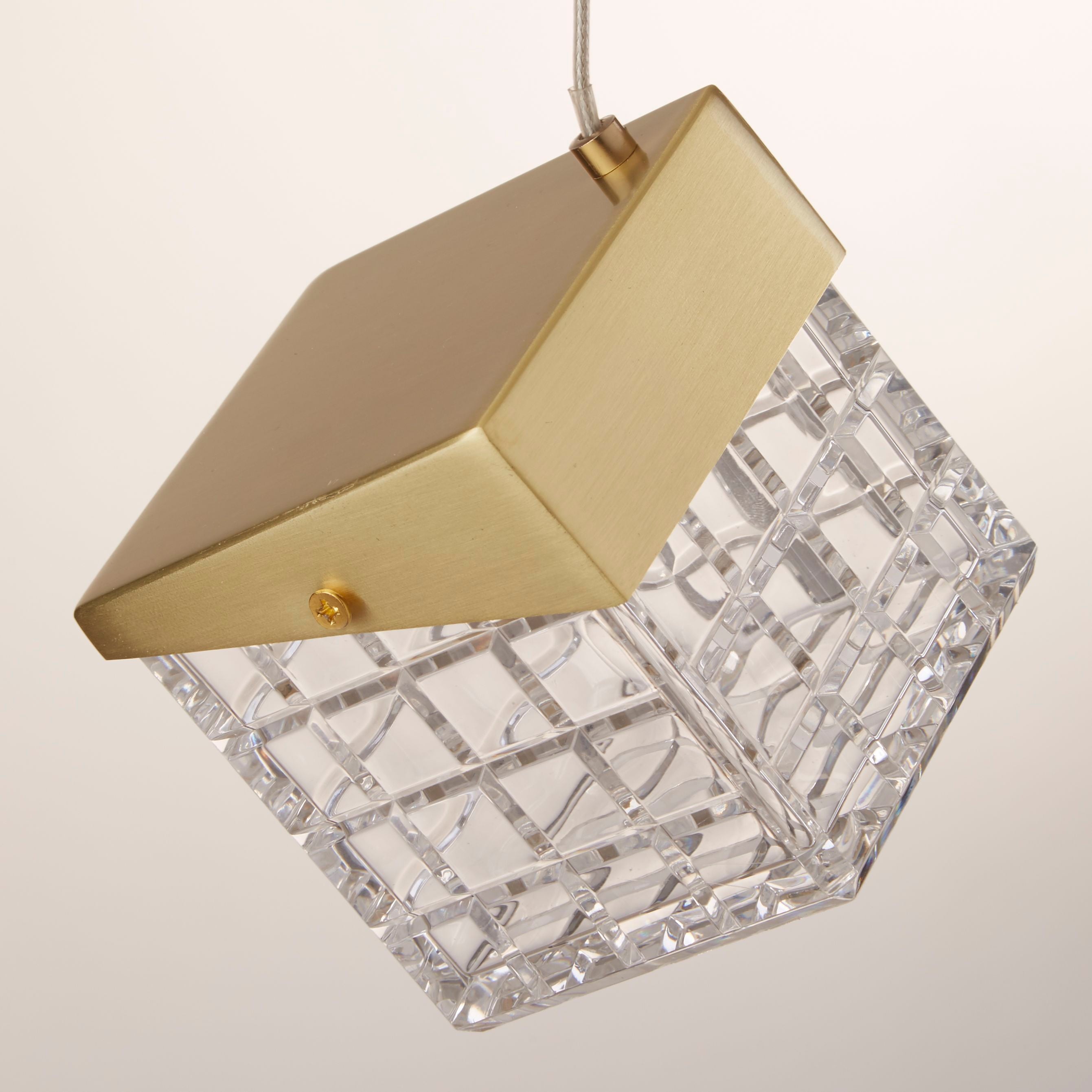 Close up of the Cuboid LED Pendant cube shade in satin brass, showing the faceted cut acrylic grid pattern and brass corner cap lit from within