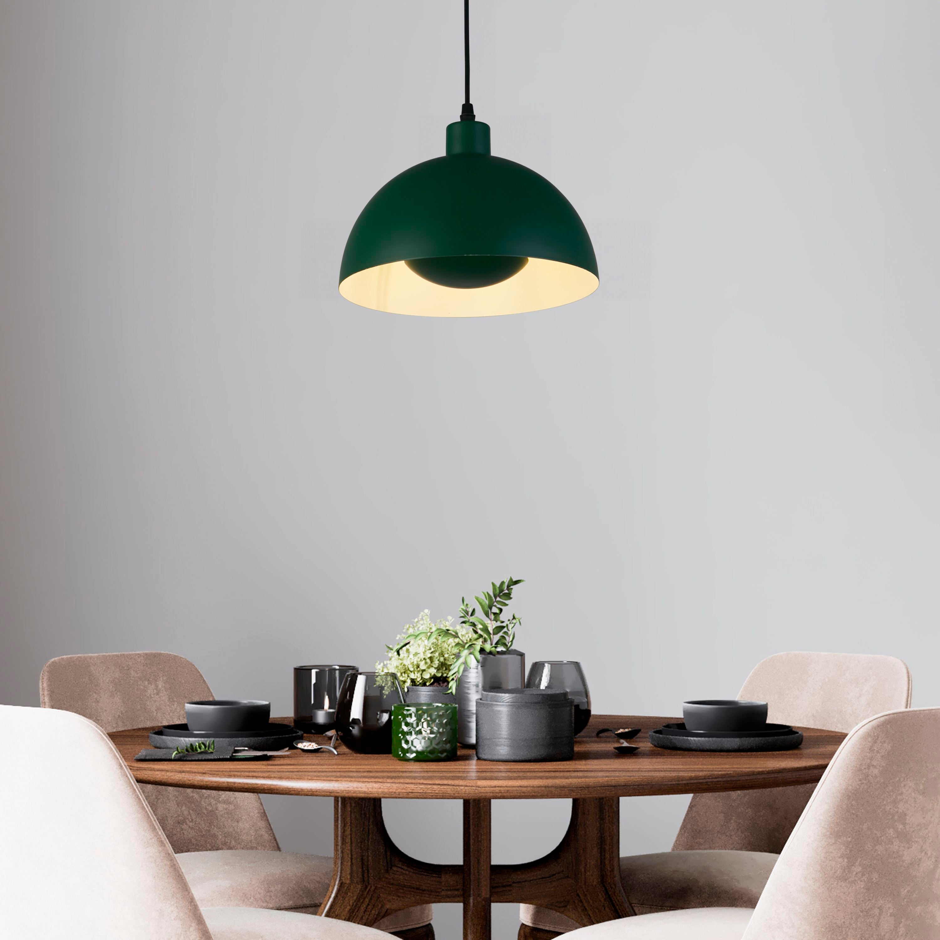 Searchlight Mars pendant in matt green metal hung above a dark wood dining table set with black tableware and greenery