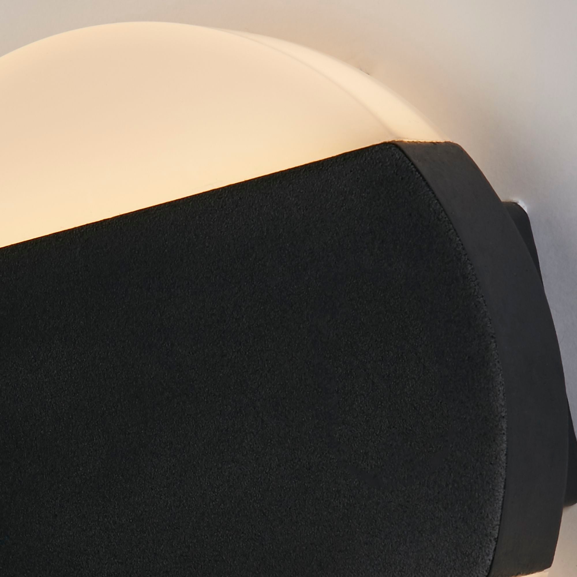 Close up of the Searchlight Cavern LED outdoor wall light showing the edge of the black band, the opal diffuser and a visible fixing screw