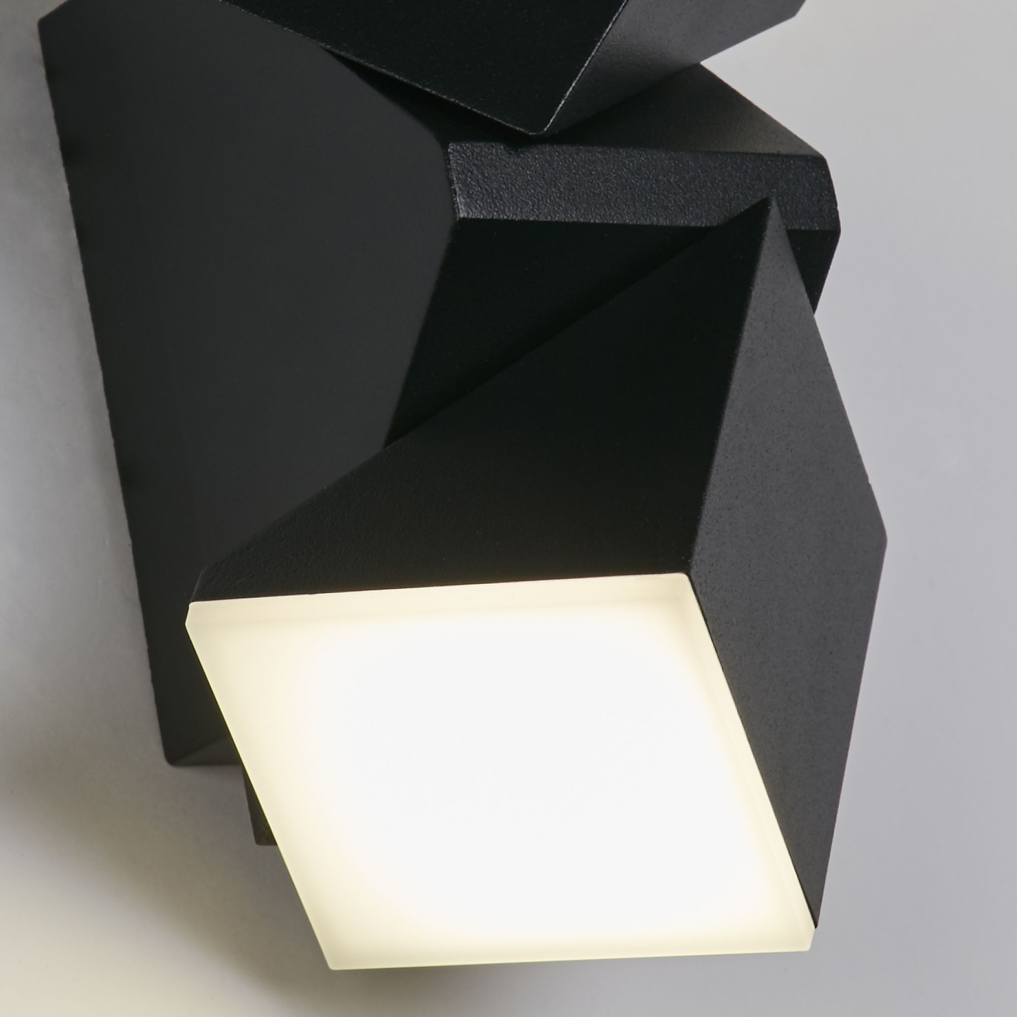 Close up of the Montana wall light's angular black housing and illuminated lens