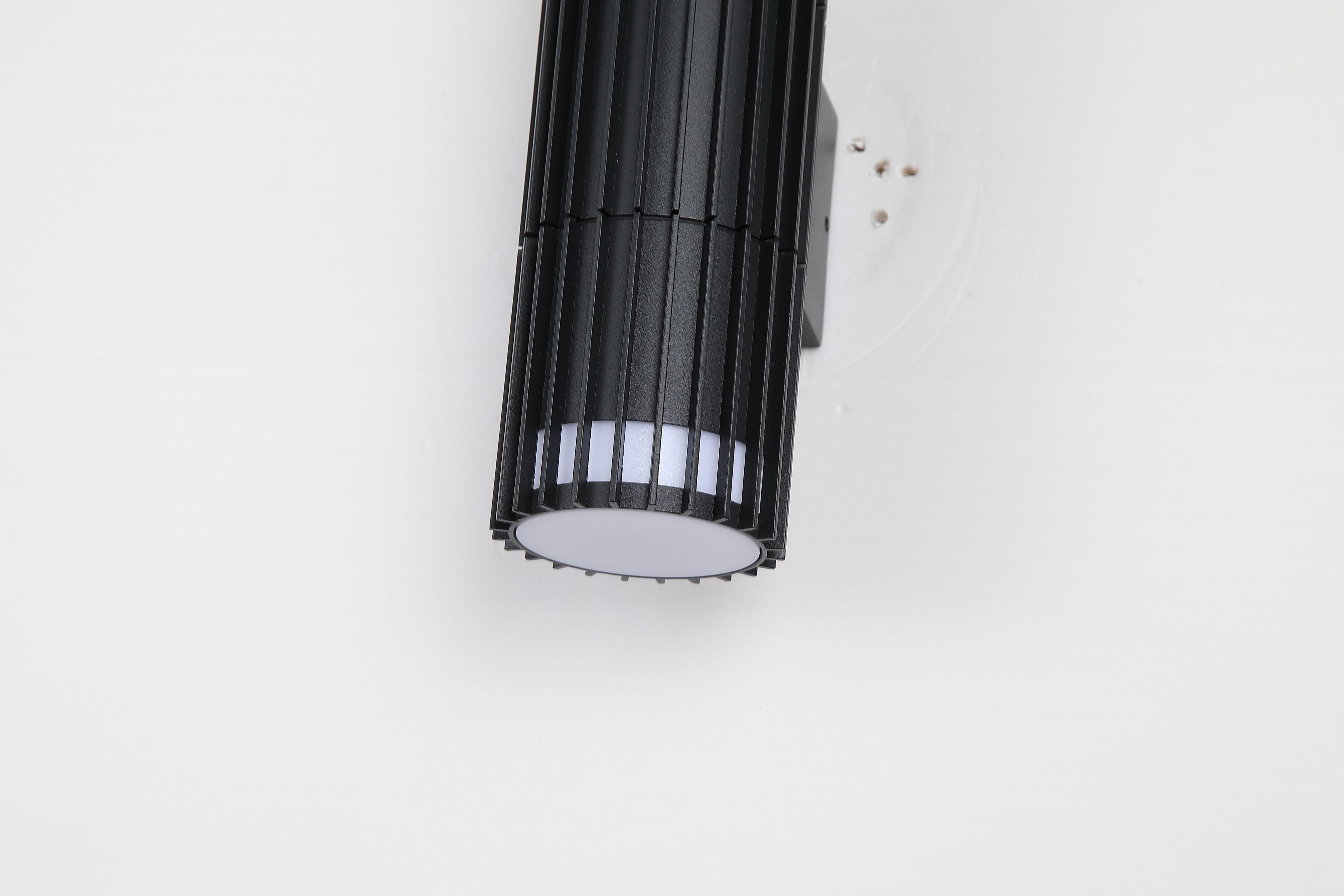 Close up angled view of the Detroit black wall light mounted on a white wall, showing the vertical fin detailing and illuminated lower vent