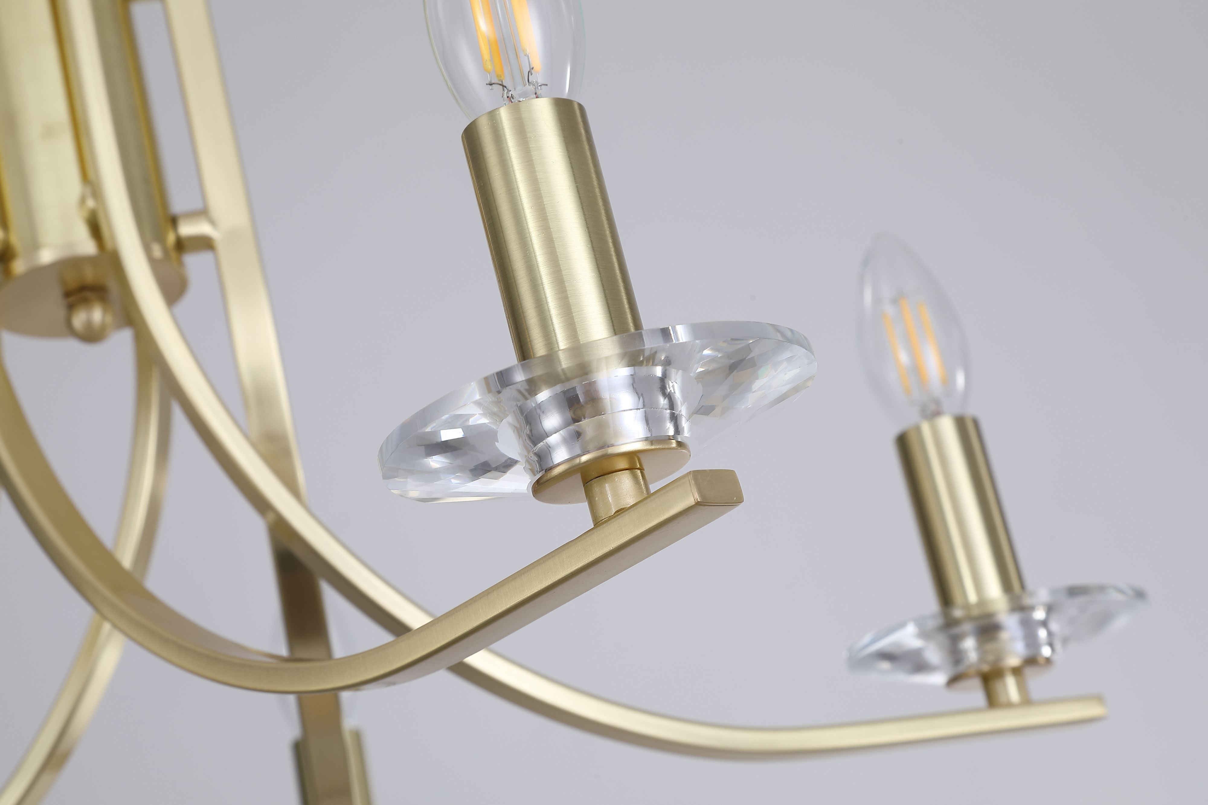 Close up of the Ascona 5 light pendant showing a candle style E14 bulb holder resting on a faceted crystal glass sconce, in satin brass