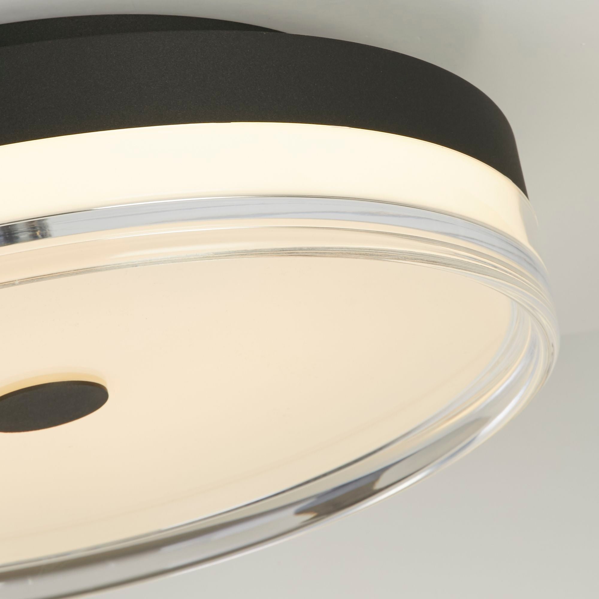 Close up of the Searchlight Cyprus LED Flush 40cm in black, showing the black metal edge, clear acrylic trim and warm glow from the diffuser