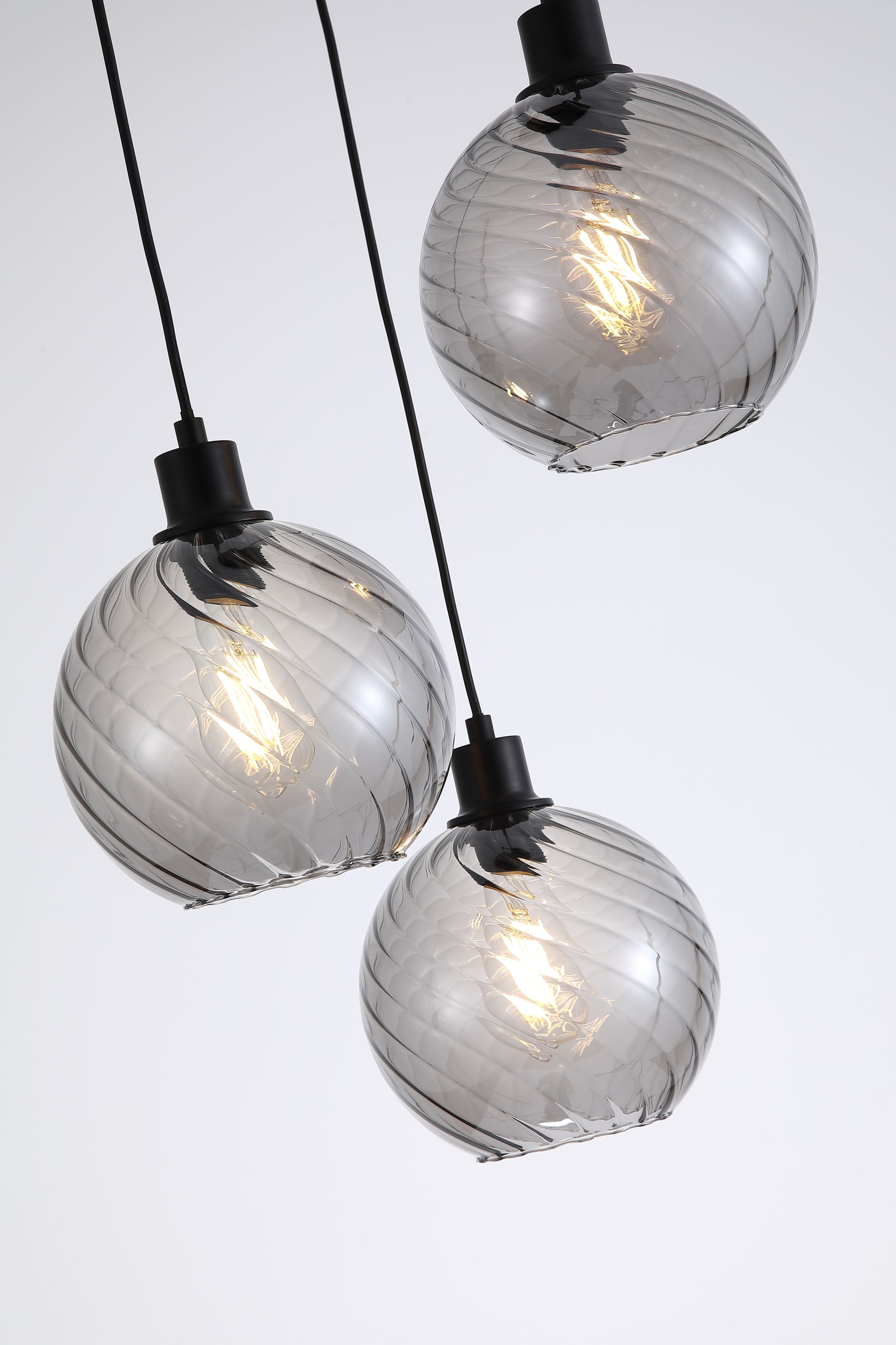 Close up of the swirled ribbed texture on the smoked glass globe shades of the Radiance 3 Light Multi Drop Pendant, showing the black fitting and filament bulb detail