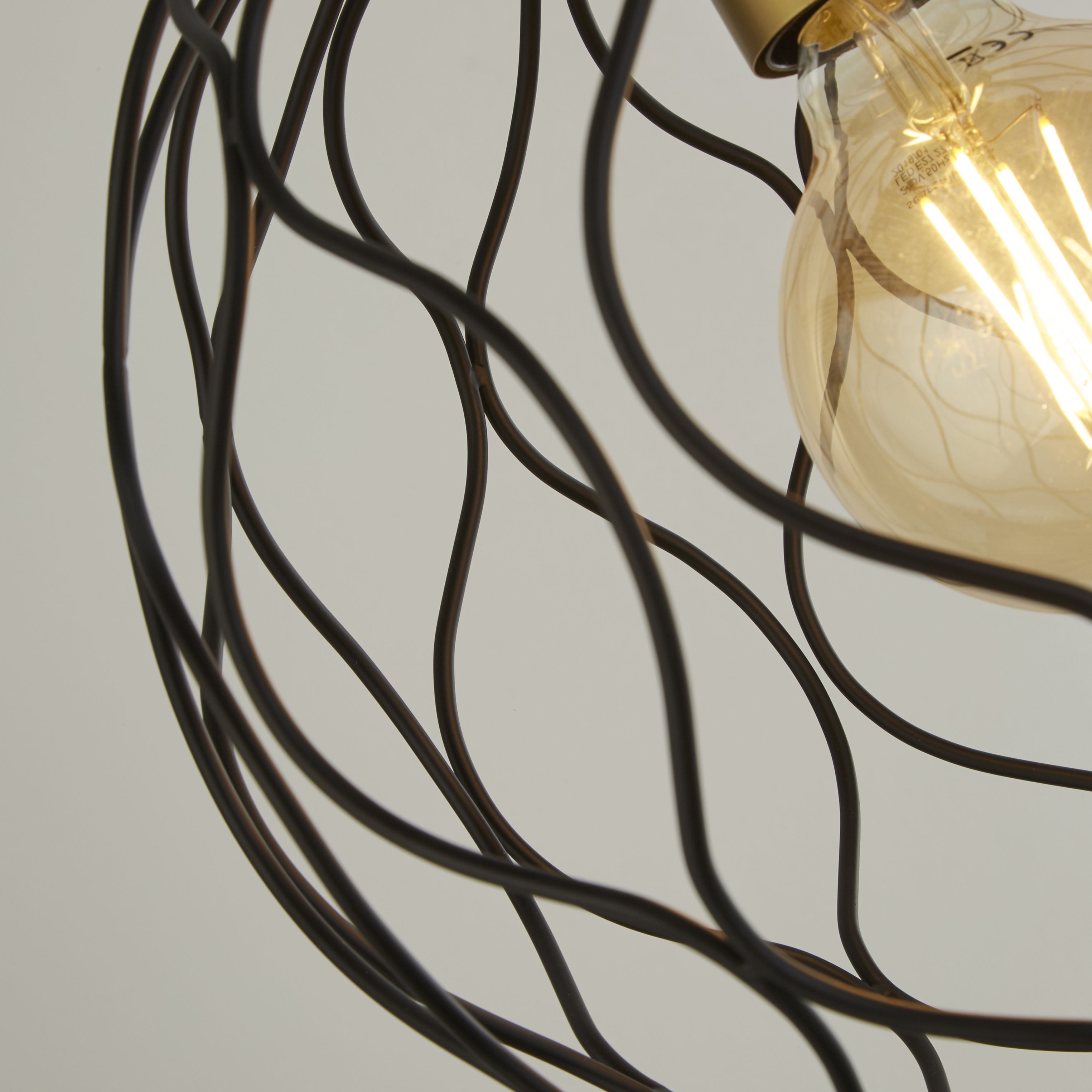 Close up detail of the Finesse pendant's wire lattice shade, showing the interwoven black wire pattern around the brass lamp holder and filament bulb