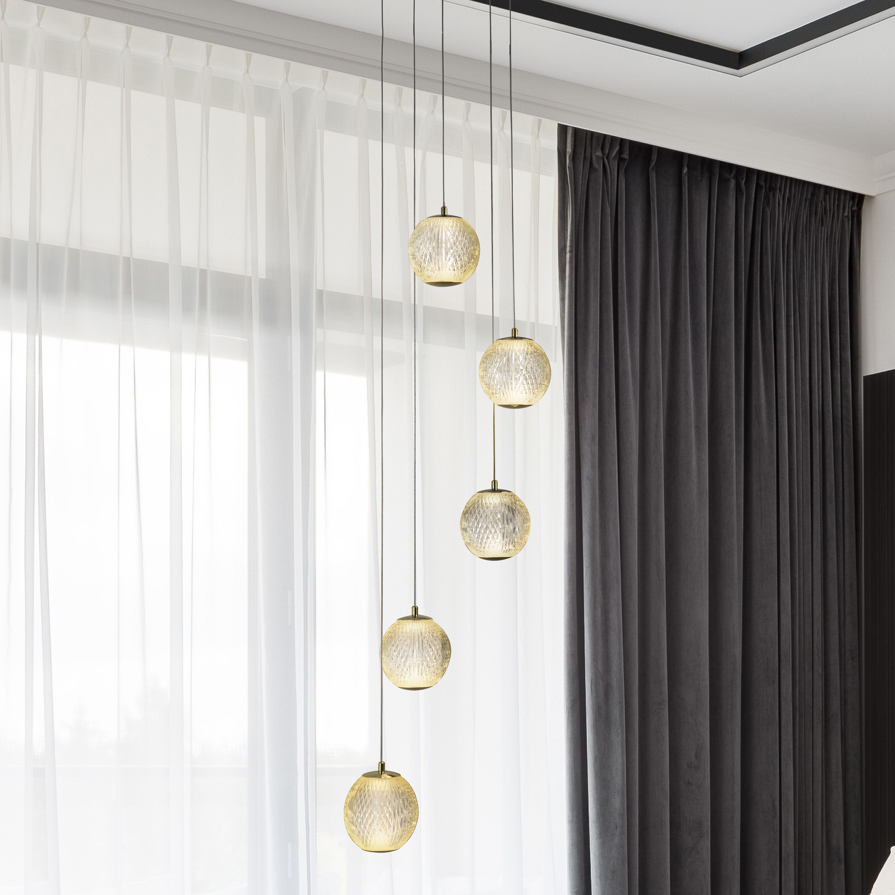 Allure 5 light multi drop pendant in satin brass styled beside sheer curtains, globes lit with a warm glow