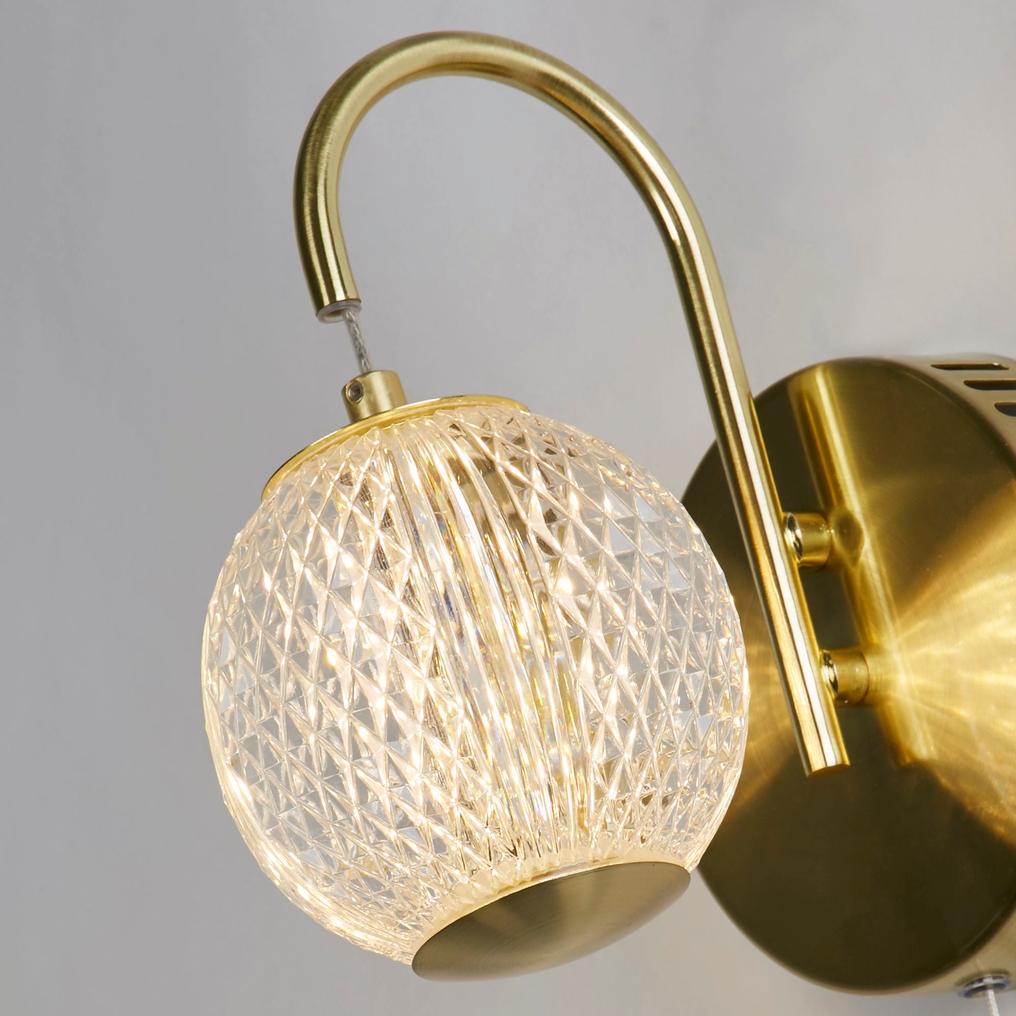 Close up of the Allure wall light's etched acrylic globe and satin brass backplate with pull cord switch